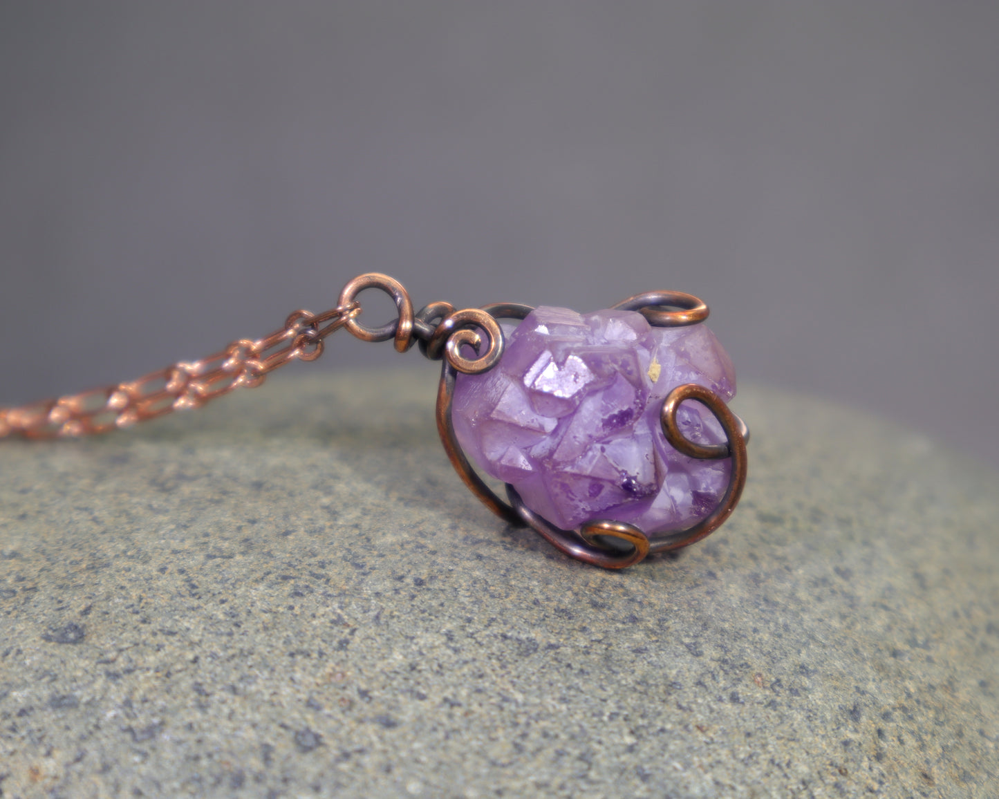 Wire-wrapped necklace with a purple amethyst crystal pendant on a gray rock