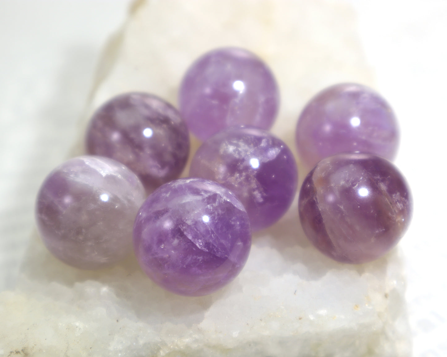 Genuine natural amethyst orbs polished gemstone spheres on a white quartz crystal base showing color variation and inclusions