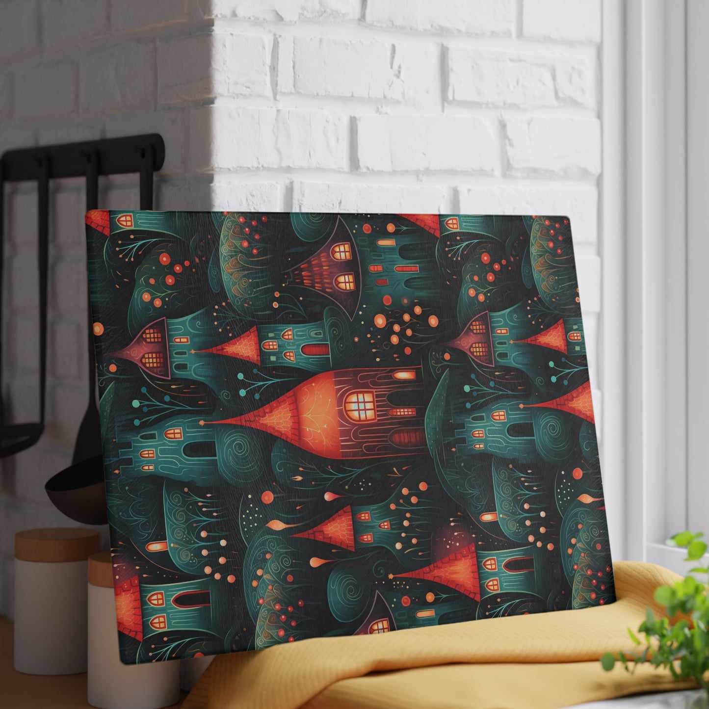 Rustic village-inspired glass cutting board propped against a white brick wall for a decorative look. This is the large size which is 11" x 15".