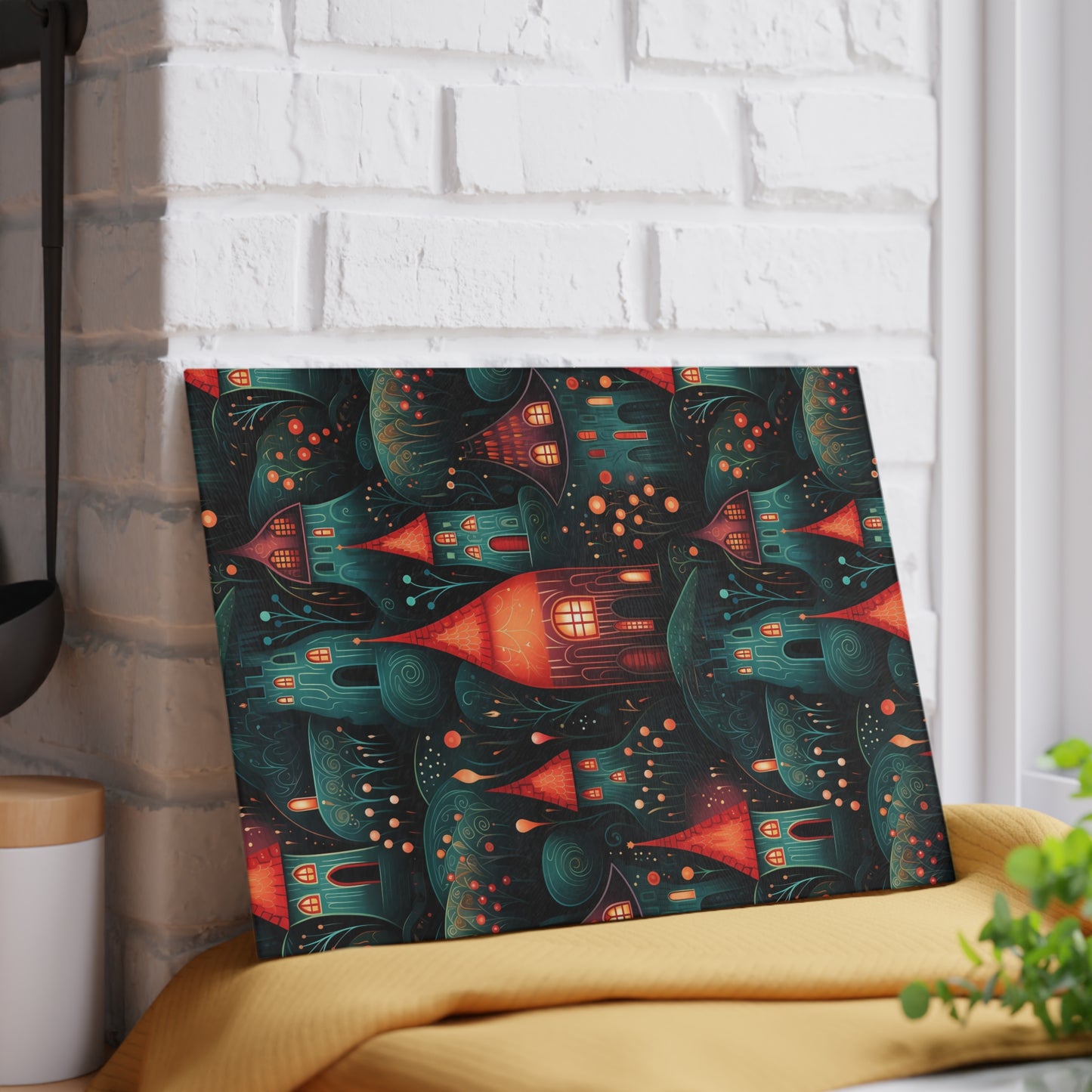 Rustic village-inspired glass cutting board propped against a white brick wall for a decorative look. Small size is 8 x 11 inches.