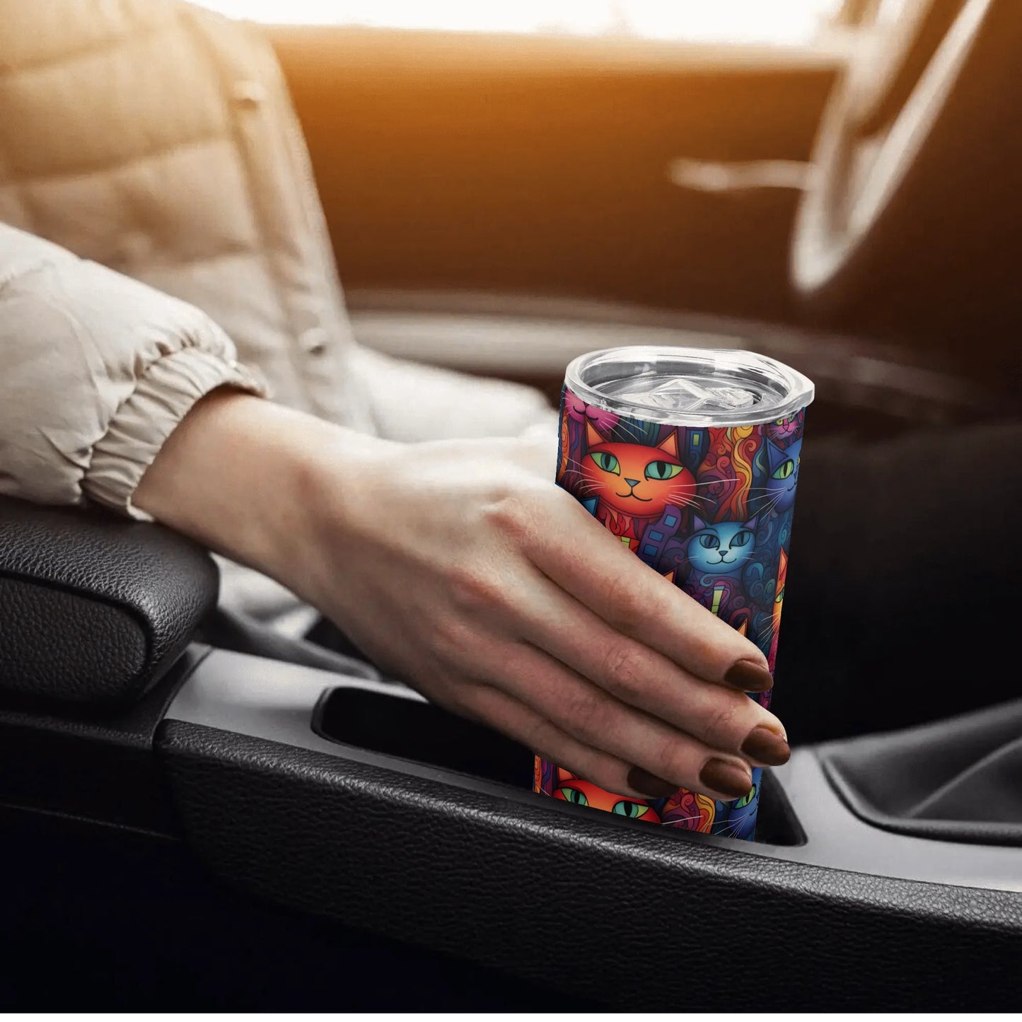 Hand holding a colorful tumbler with cat designs inside a car.