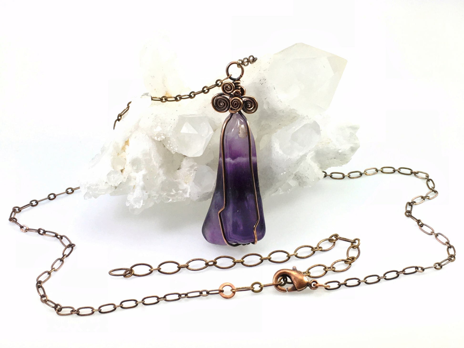 Handmade purple chevron amethyst crystal necklace displayed on quartz crystal cluster