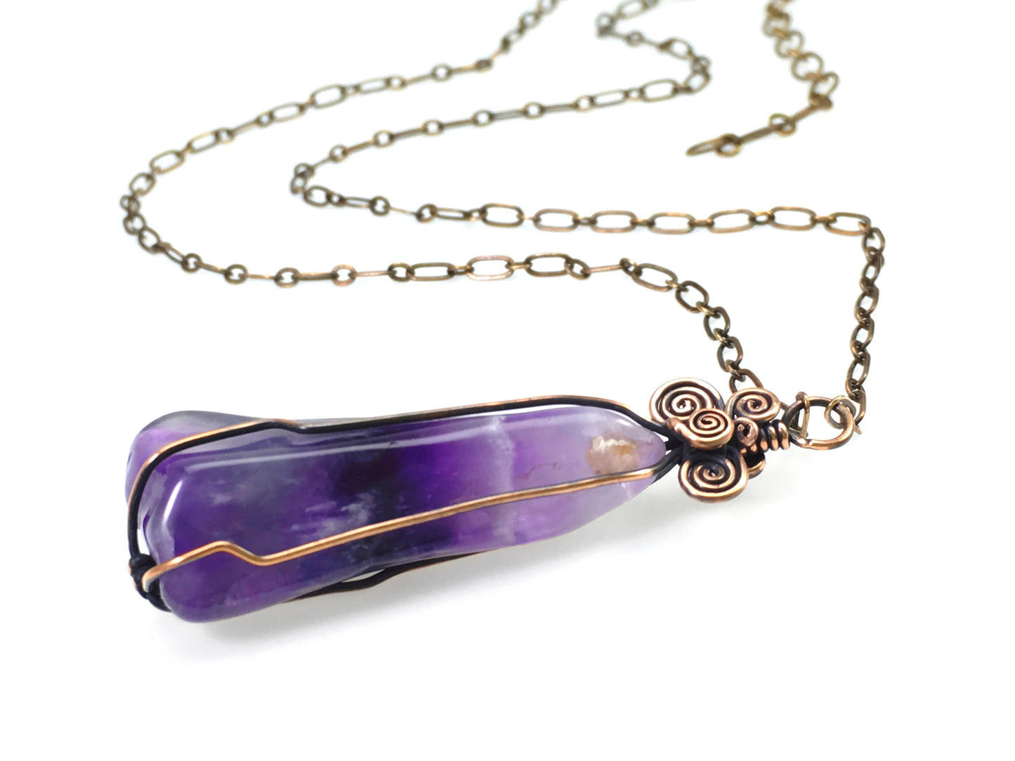 Side view of natural chevron amethyst gemstone pendant wrapped in copper wire