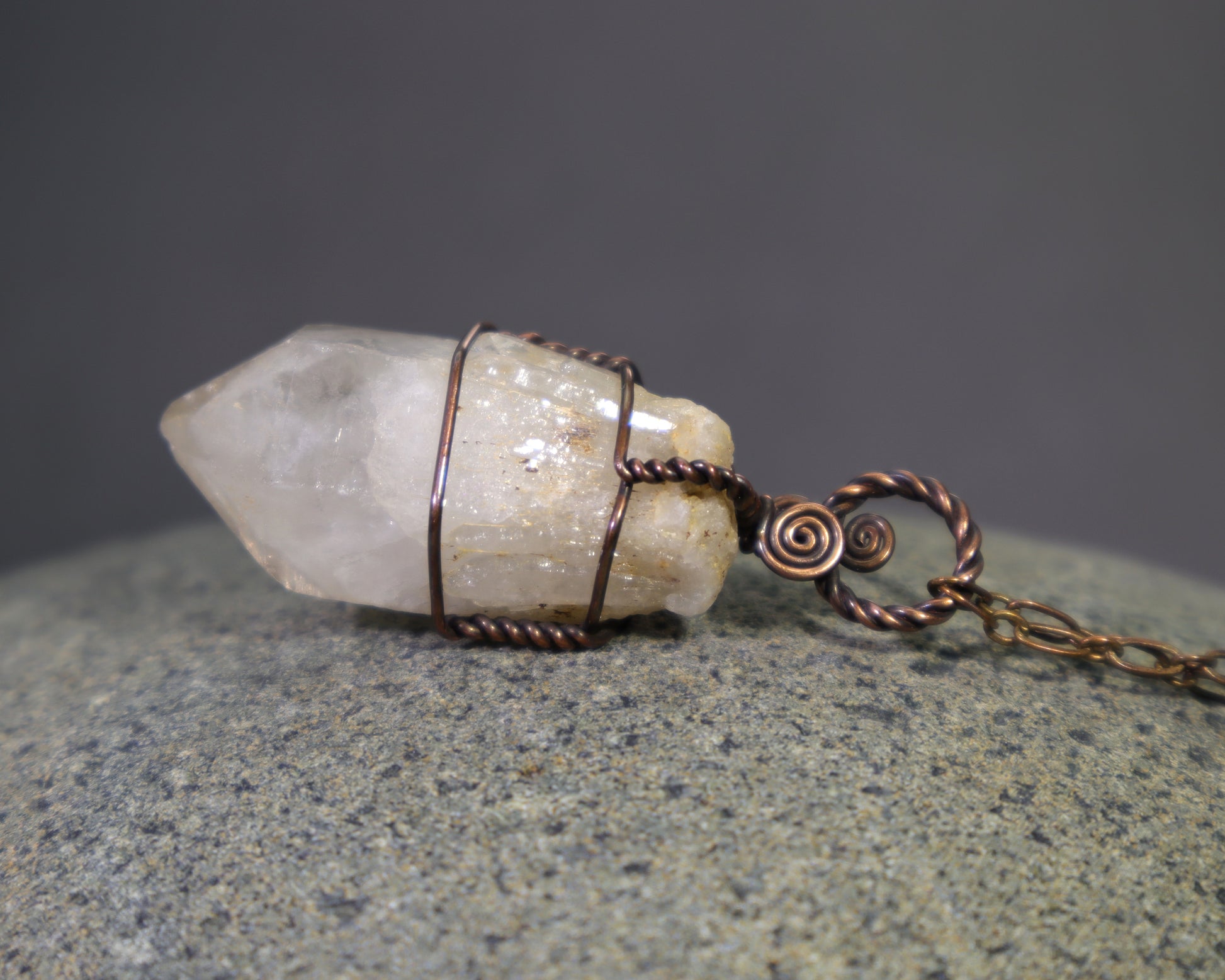 Raw natural citrine crystal pendant featuring unheated phantom candle quartz wire wrapped in oxidized copper.  The pendant sits on a stone surface.