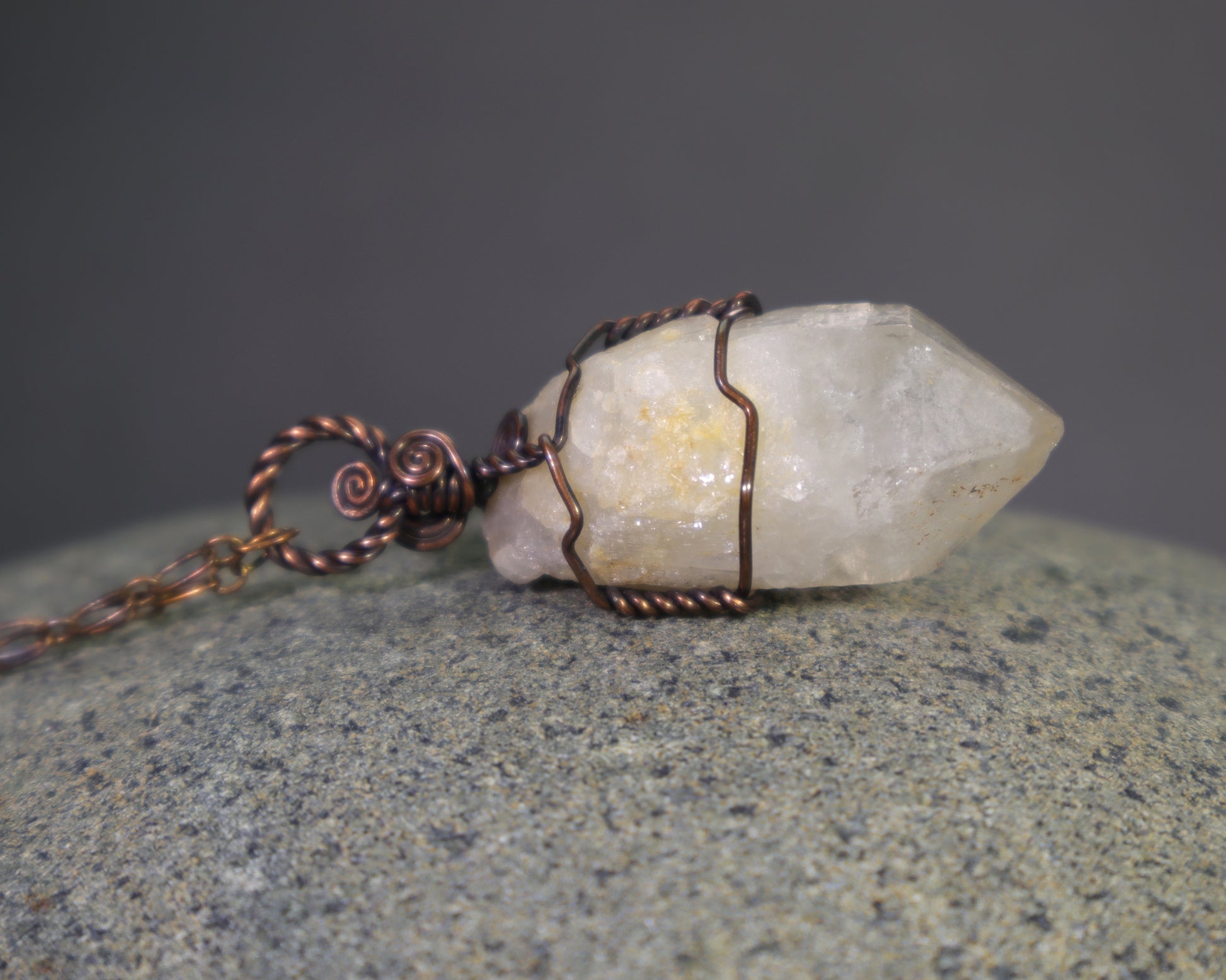 Raw natural citrine crystal pendant featuring unheated phantom candle quartz wire wrapped in oxidized copper laying on a large rock