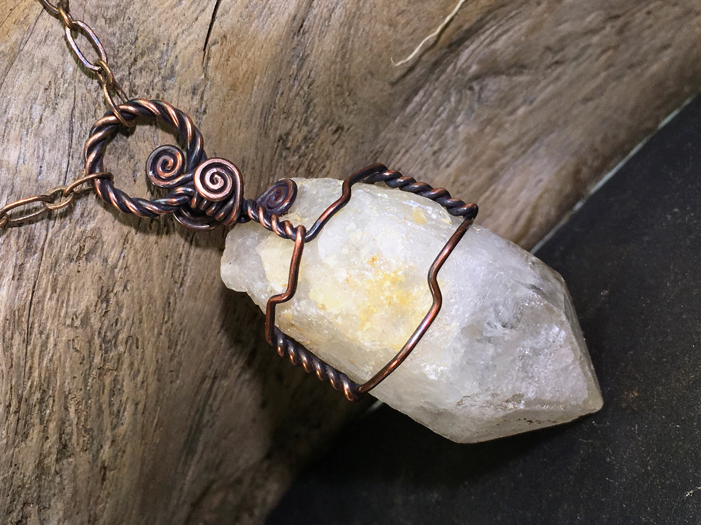 Copper wire-wrapped pendant on a genuine citrine crystal with a kaolinite phantom photographed on a natural wood background
