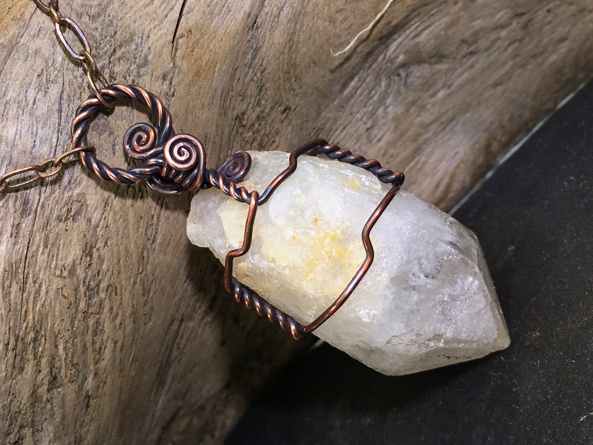Copper wire-wrapped pendant on a genuine citrine crystal with a kaolinite phantom photographed on a natural wood background