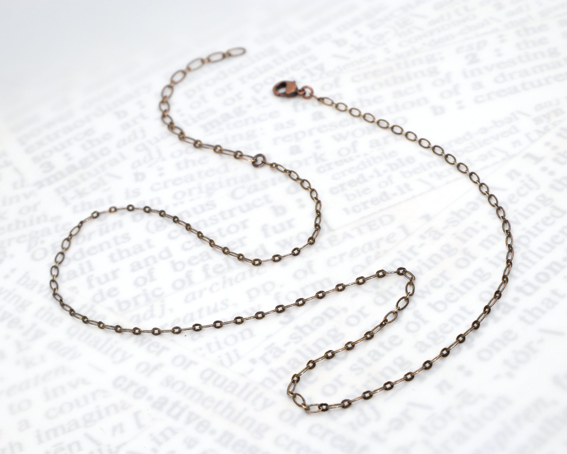Antiqued copper flat link chain necklace with an adjustable extender chain on a textured white background