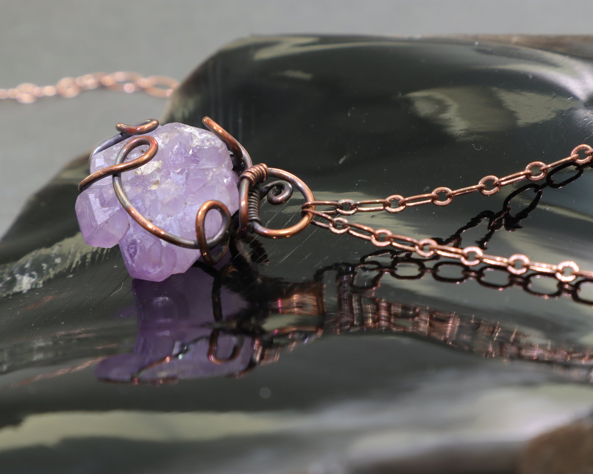 Handmade elestial amethyst necklace with rustic oxidized copper wire wrapping on a chunk of obsidian.