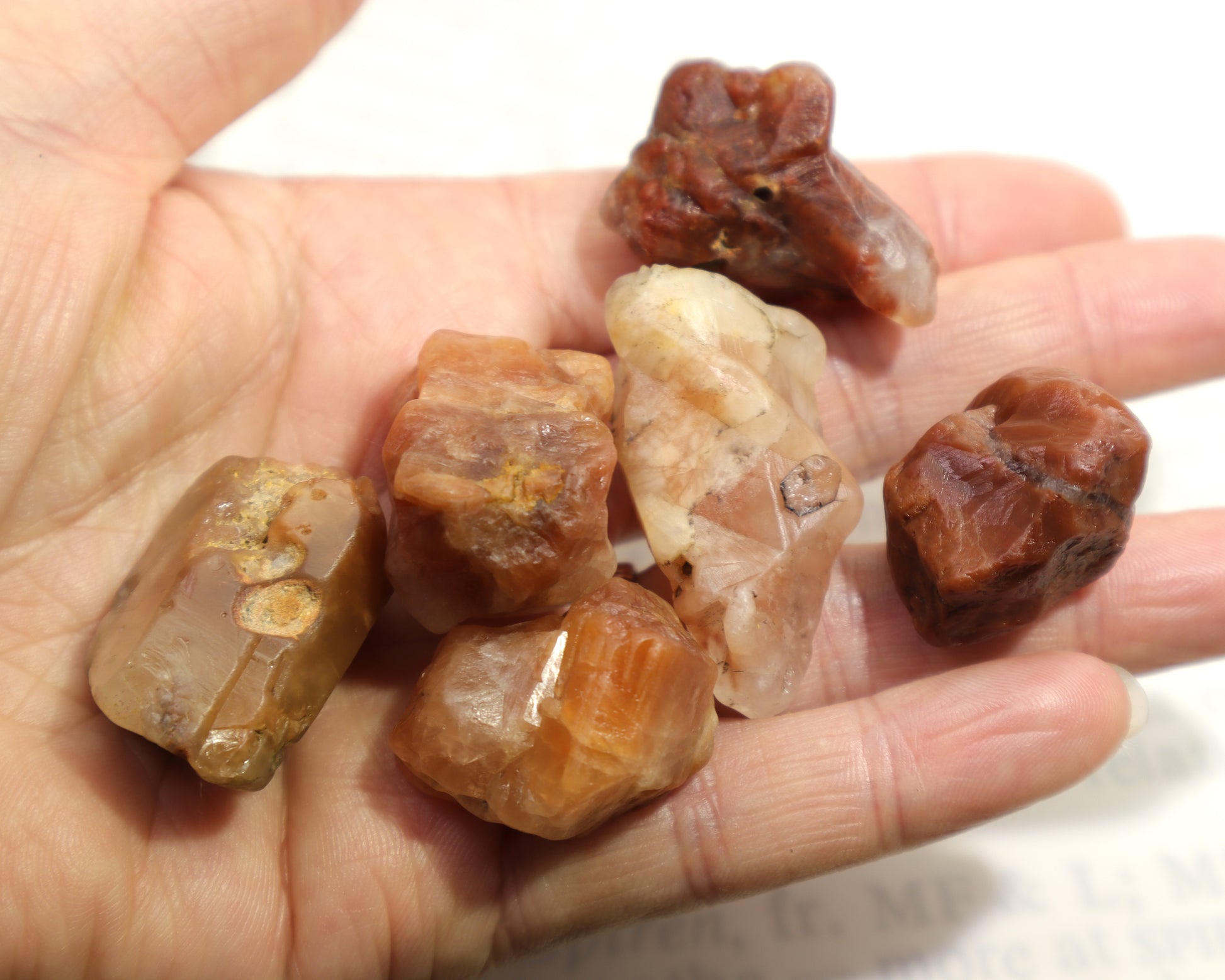 Hematoid quartz crystal in hand showing internal phantom structure and various colors from peach to orange, brown and red.