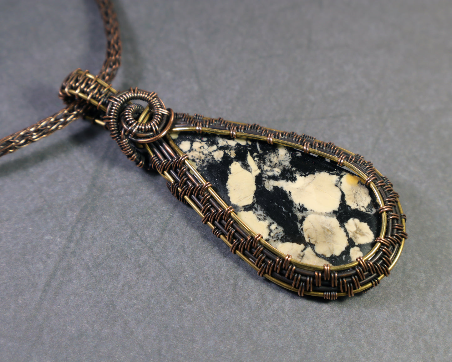 Front view of magnesite cabochon wire wrapped pendant on a dark gray background