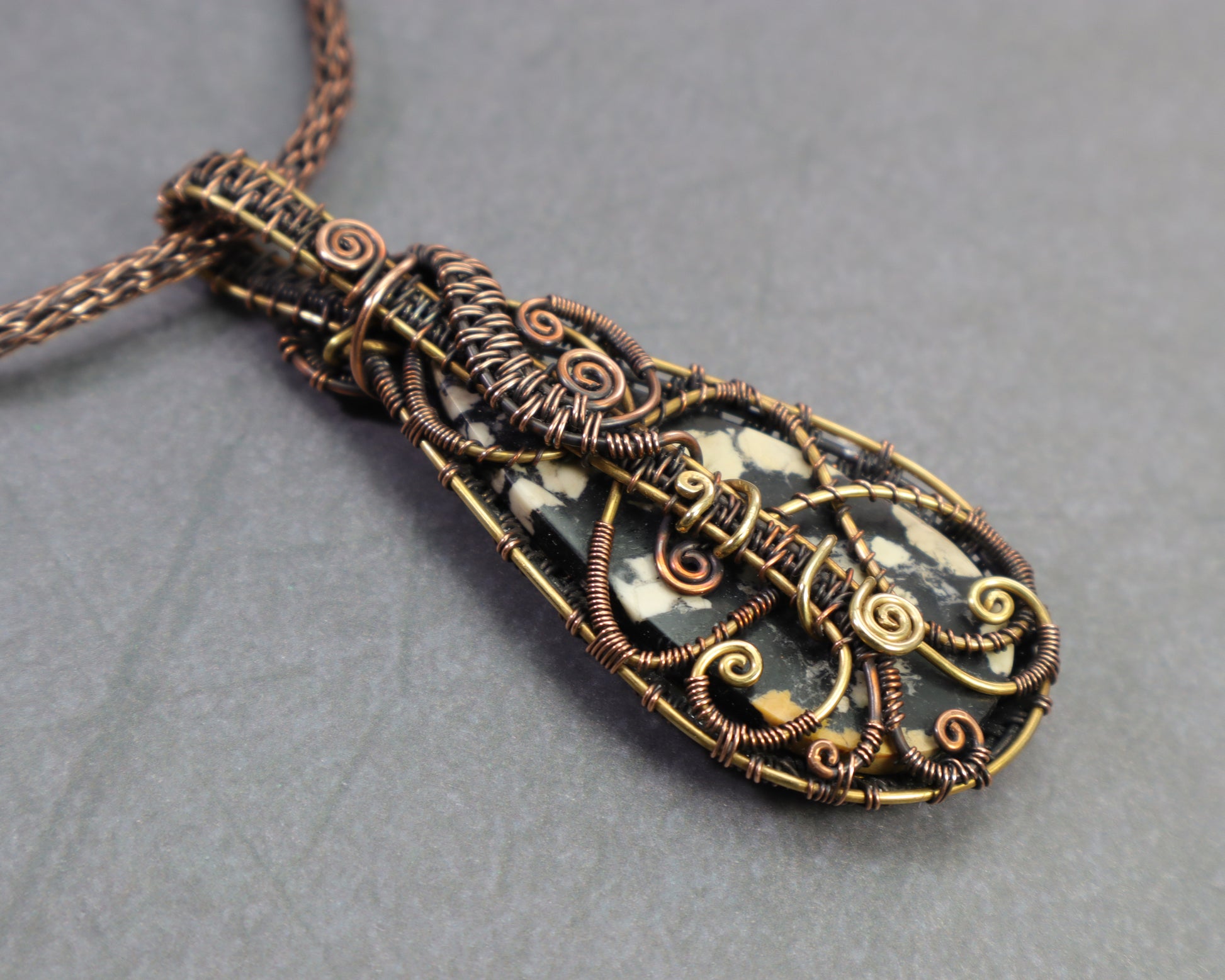 Back side of black and ivory patterned magnesite gemstone in handcrafted setting with labyrinth wire-work