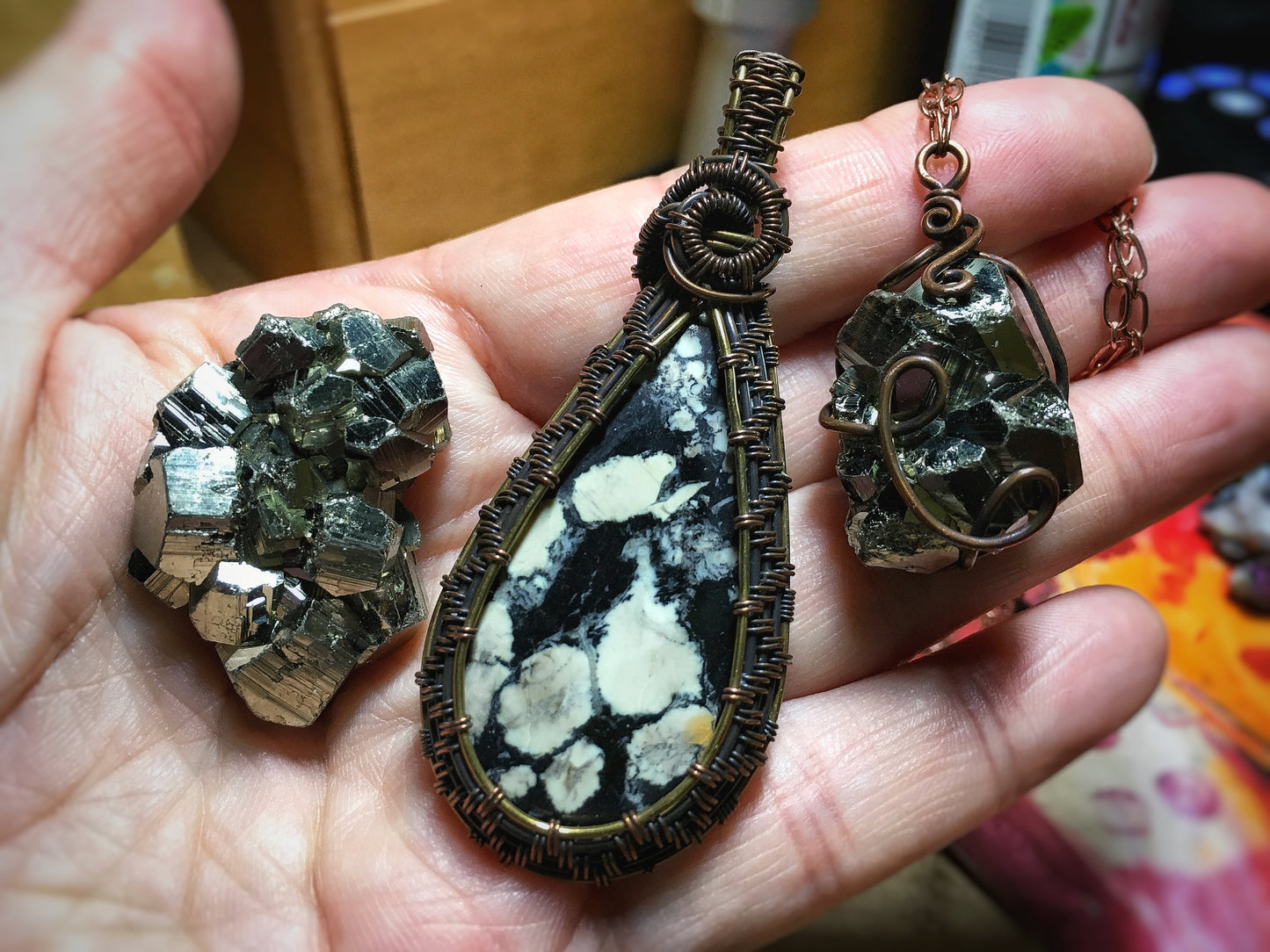 Hand holding two pendants with intricate designs and a pyrite crystal on a blurred background