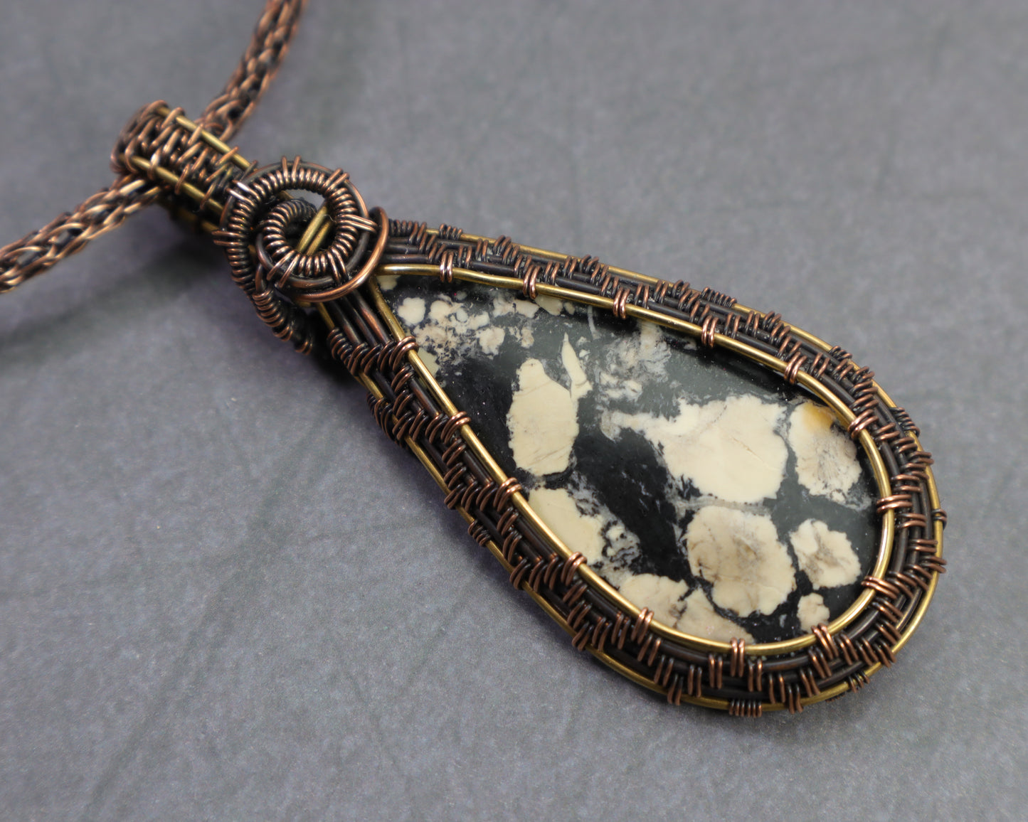 Magnesite map pendant wire wrapped in copper and brass on a dark gray background.