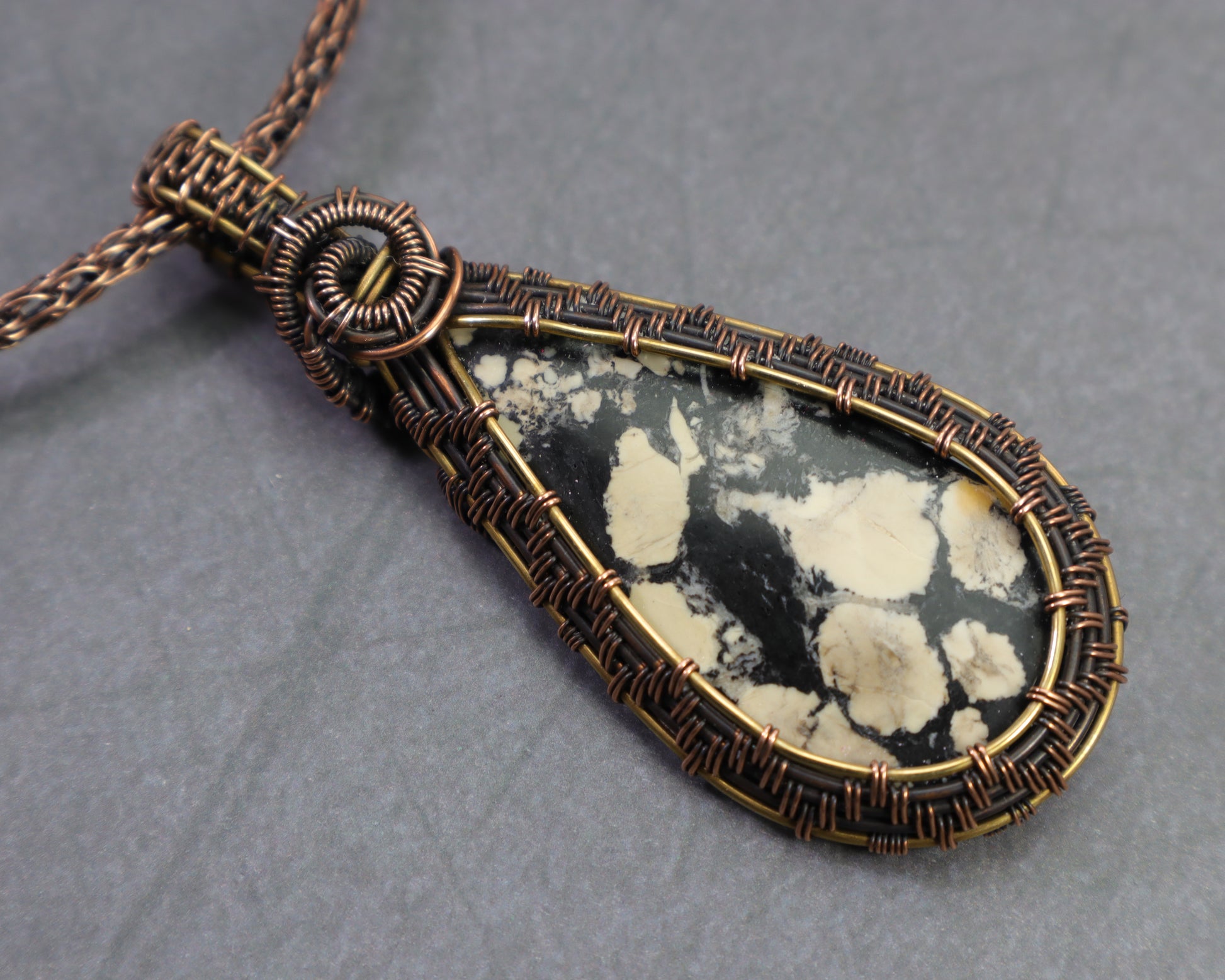Magnesite map pendant wire wrapped in copper and brass on a dark gray background.