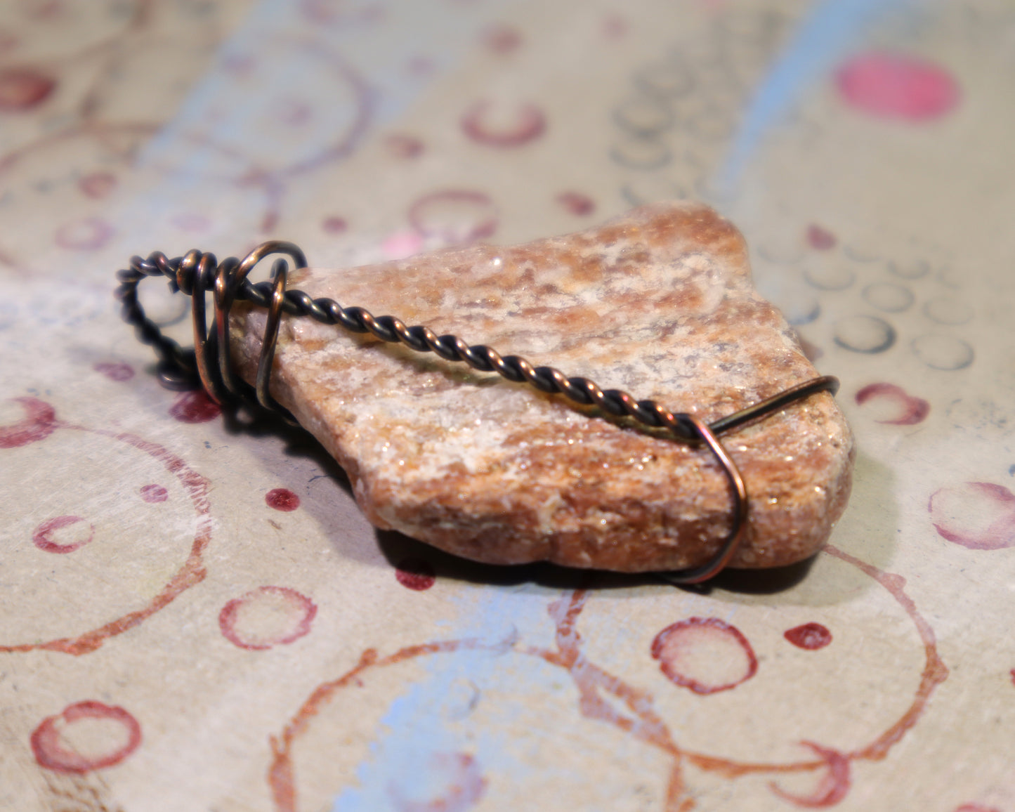 Back side of handmade copper wire wrapped pegmatite stone jewelry for geologists.