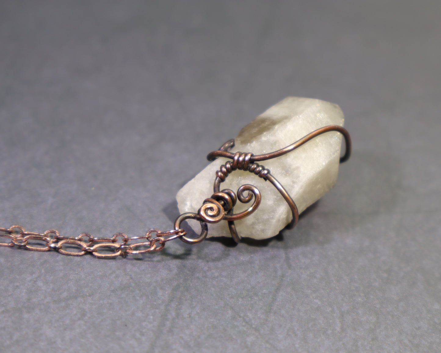 Top view of raw phantom citrine crystal pendant displayed with copper chain on gray background