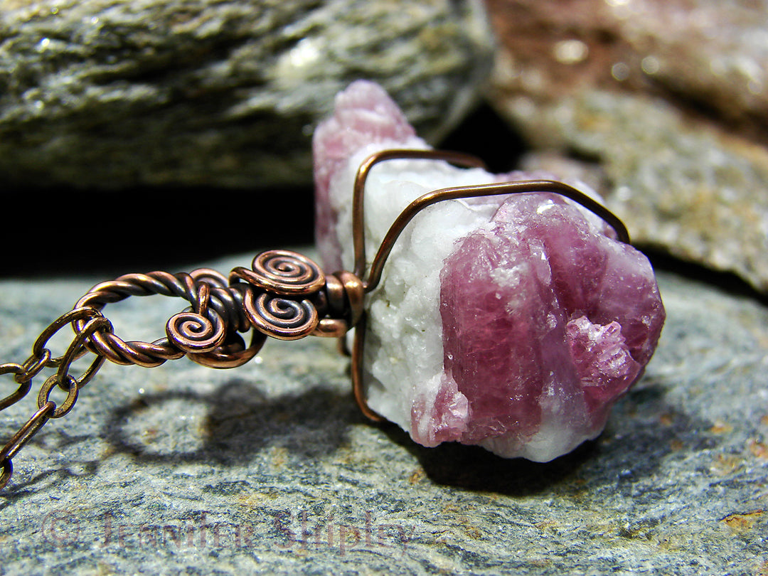 Necklace with a pink tourmaline in white albite crystal pendant on a rock surface.