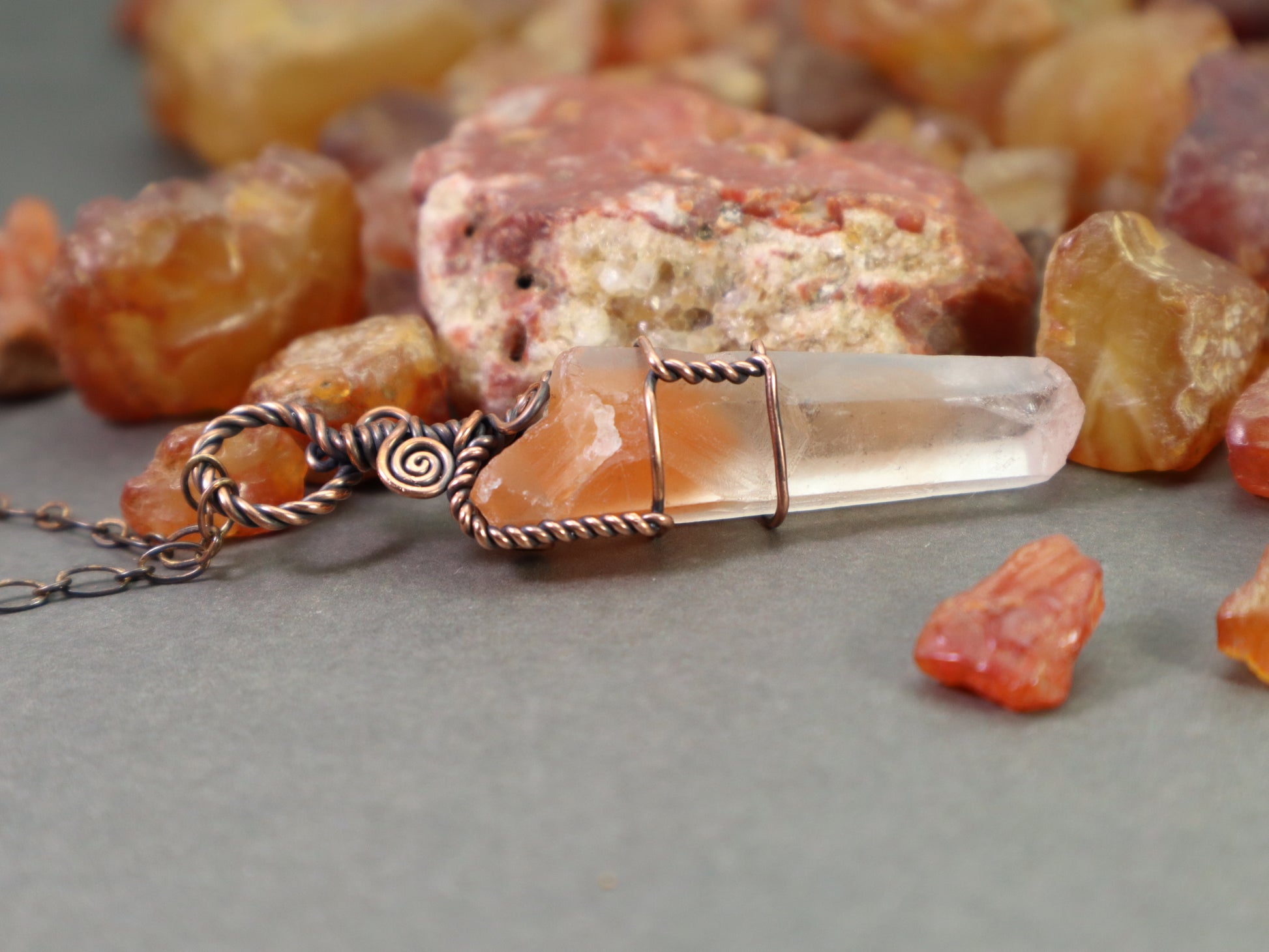 Grounding crystal necklace with red phantom quartz and copper wirework photographed on a gray background with natural carnelians rockhounded in washington state
