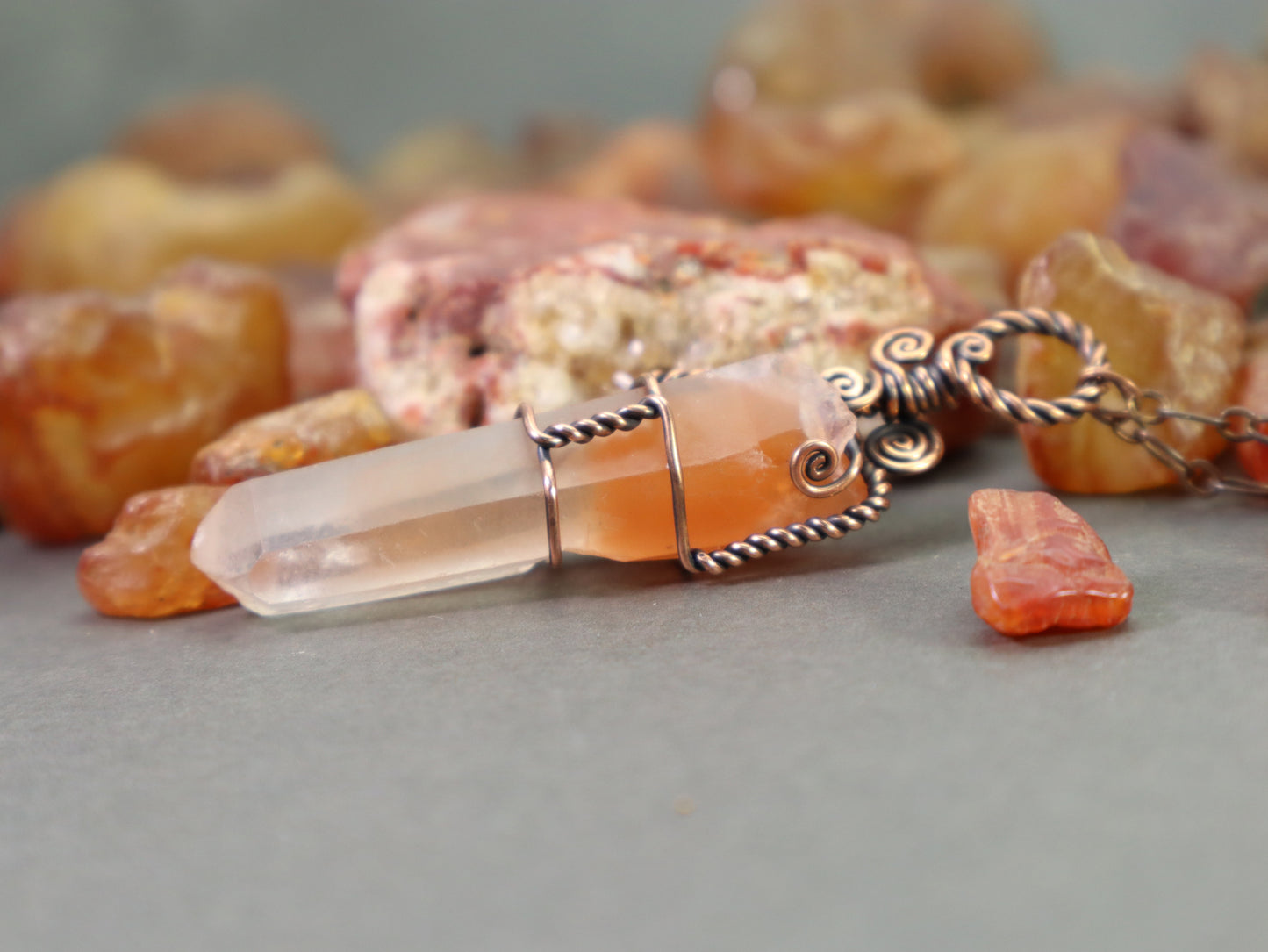 Orange hematite included quartz crystal pendant wire wrapped in copper shown with raw washington state carnelians.