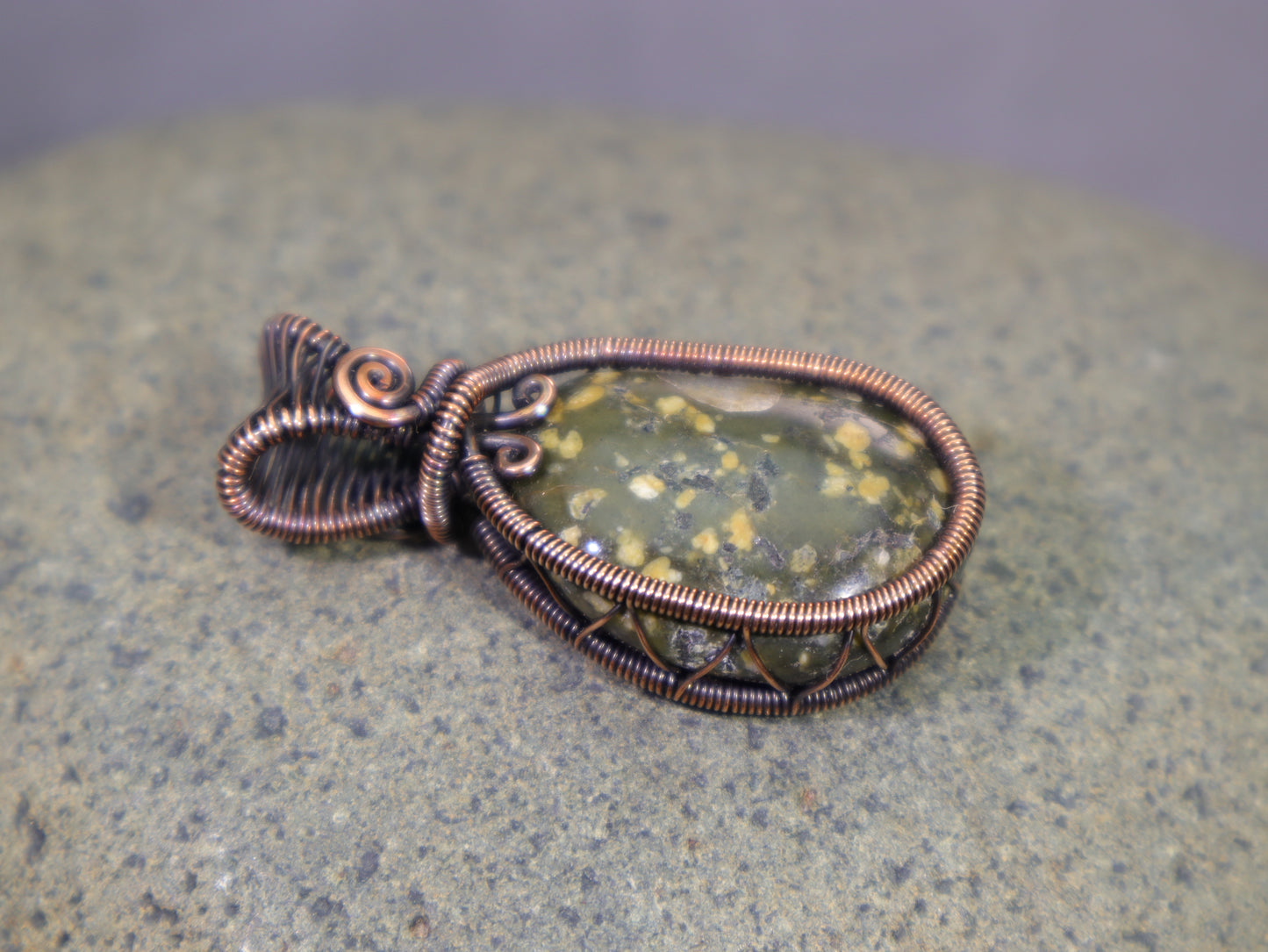 Beachcombed green jasper gemstone wrapped in oxidized copper photographed on an igneous rock.