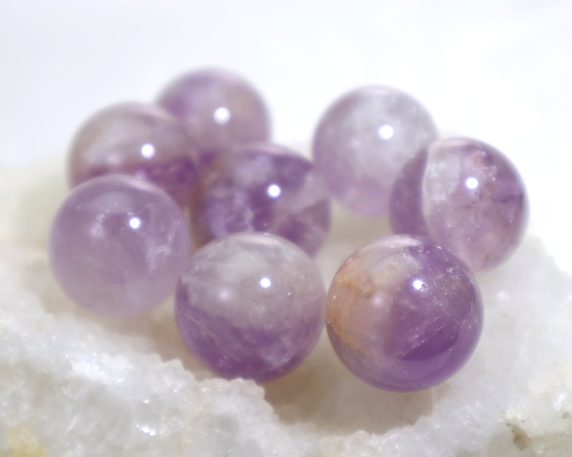 Close-up of amethyst crystal ball lot showing color variation sitting on a clear quartz cluster