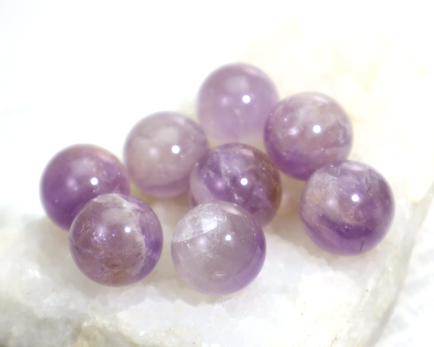 Amethyst sphere lot on a white crystal background showing color variation and some smoky tones