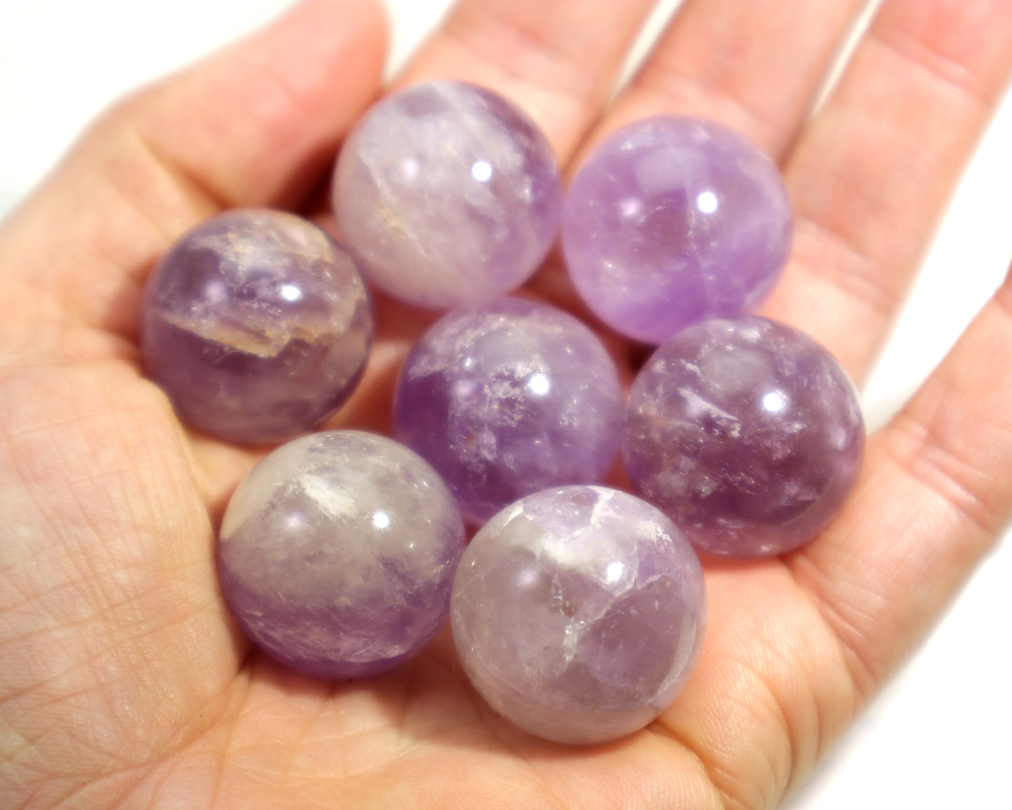 Hand holding violet amethyst crystal balls against a white background