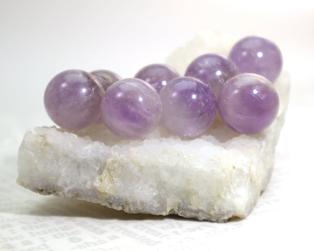 Purple amethyst crystal balls sitting on a quartz crystal cluster on a white background