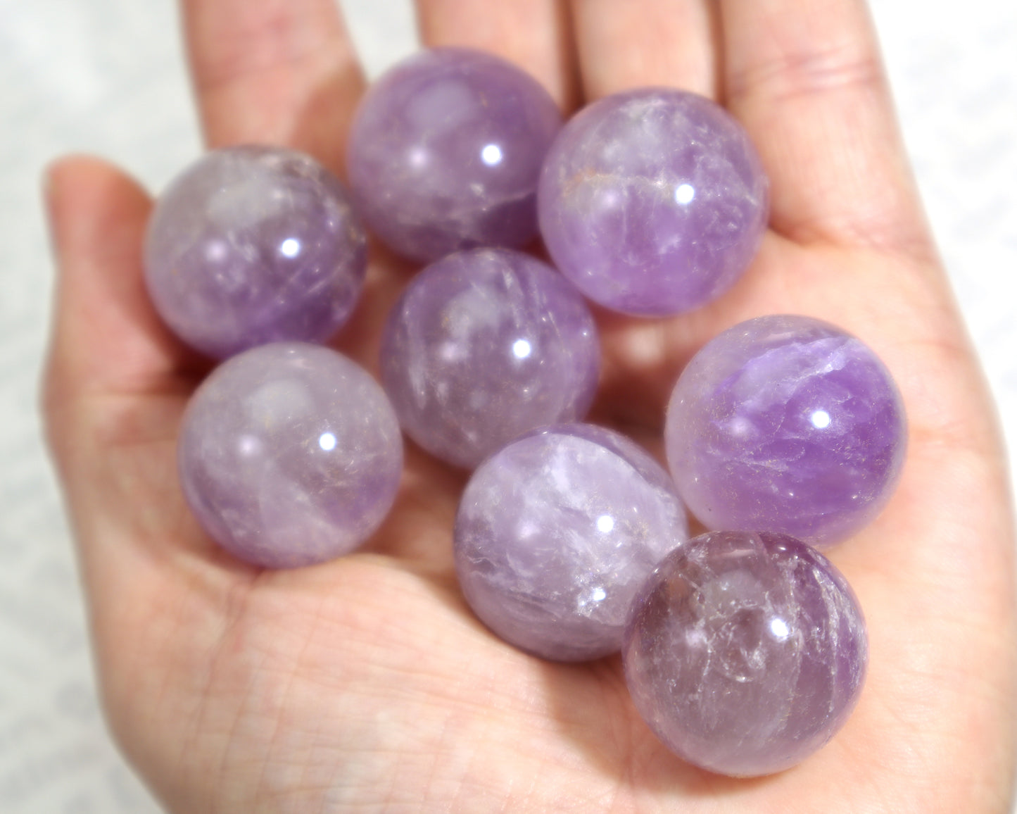 Hand holding small purple amethyst orbs against a white background perfect for wire wrapping