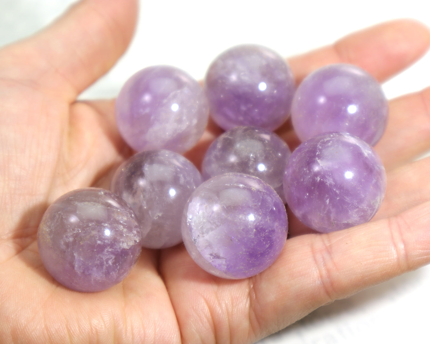 Hand holding small amethyst spheres for Reiki and chakra healing against a white background