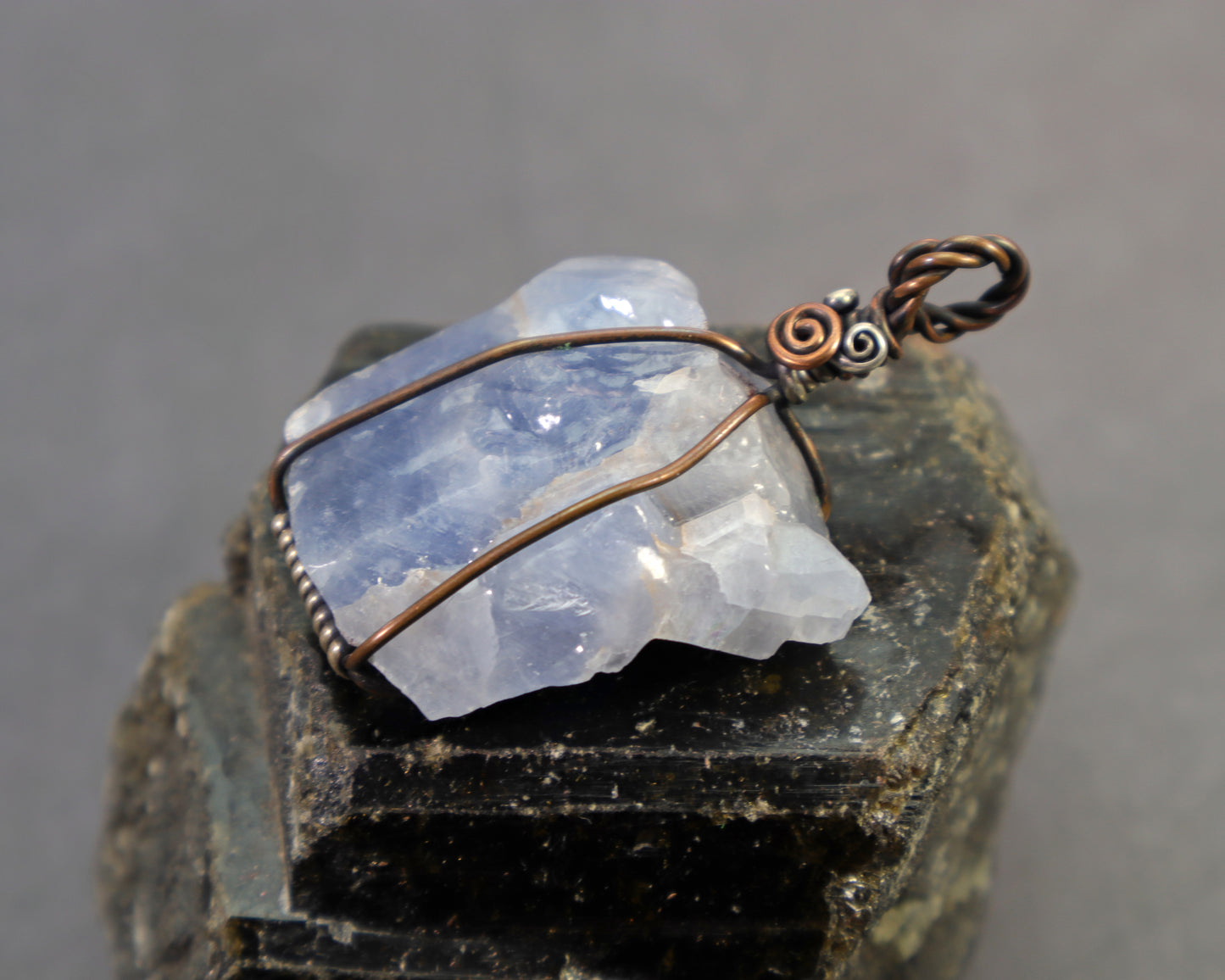 Raw blue calcite crystal pendant with art nouveau inspired wire wrapping sitting on to of a large black tourmaline crystal