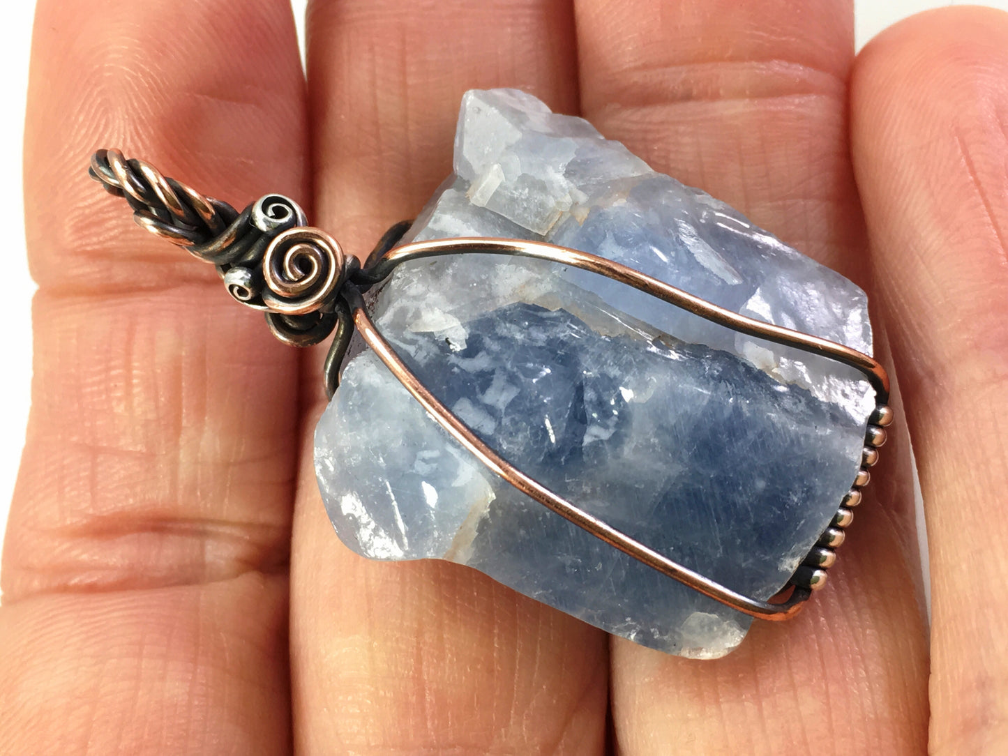 Raw blue calcite crystal pendant with art nouveau inspired wire wrapping held in hand