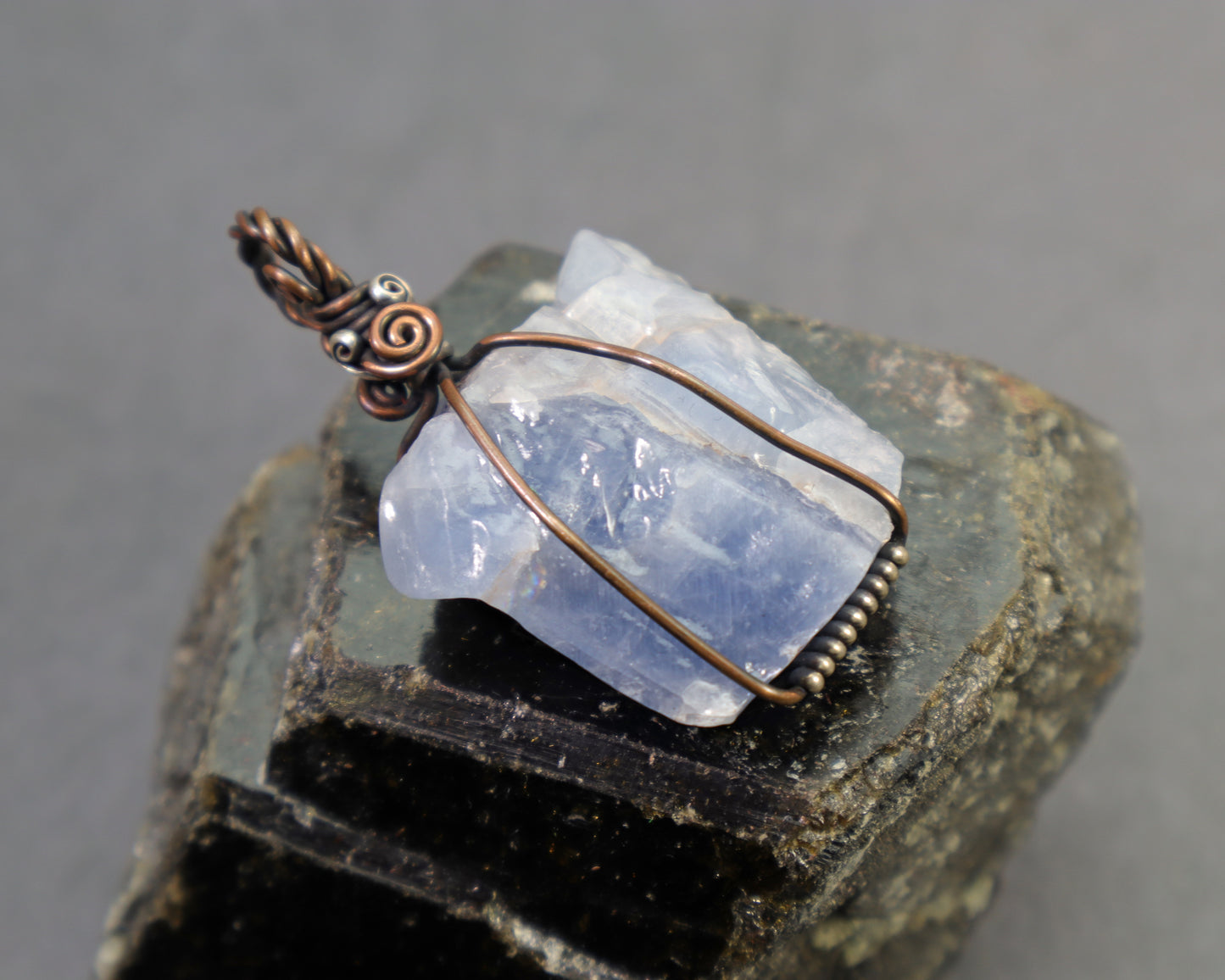 Blue calcite healing crystal pendant made with nickel free copper and silver sitting on top of a large black tourmaline crystal