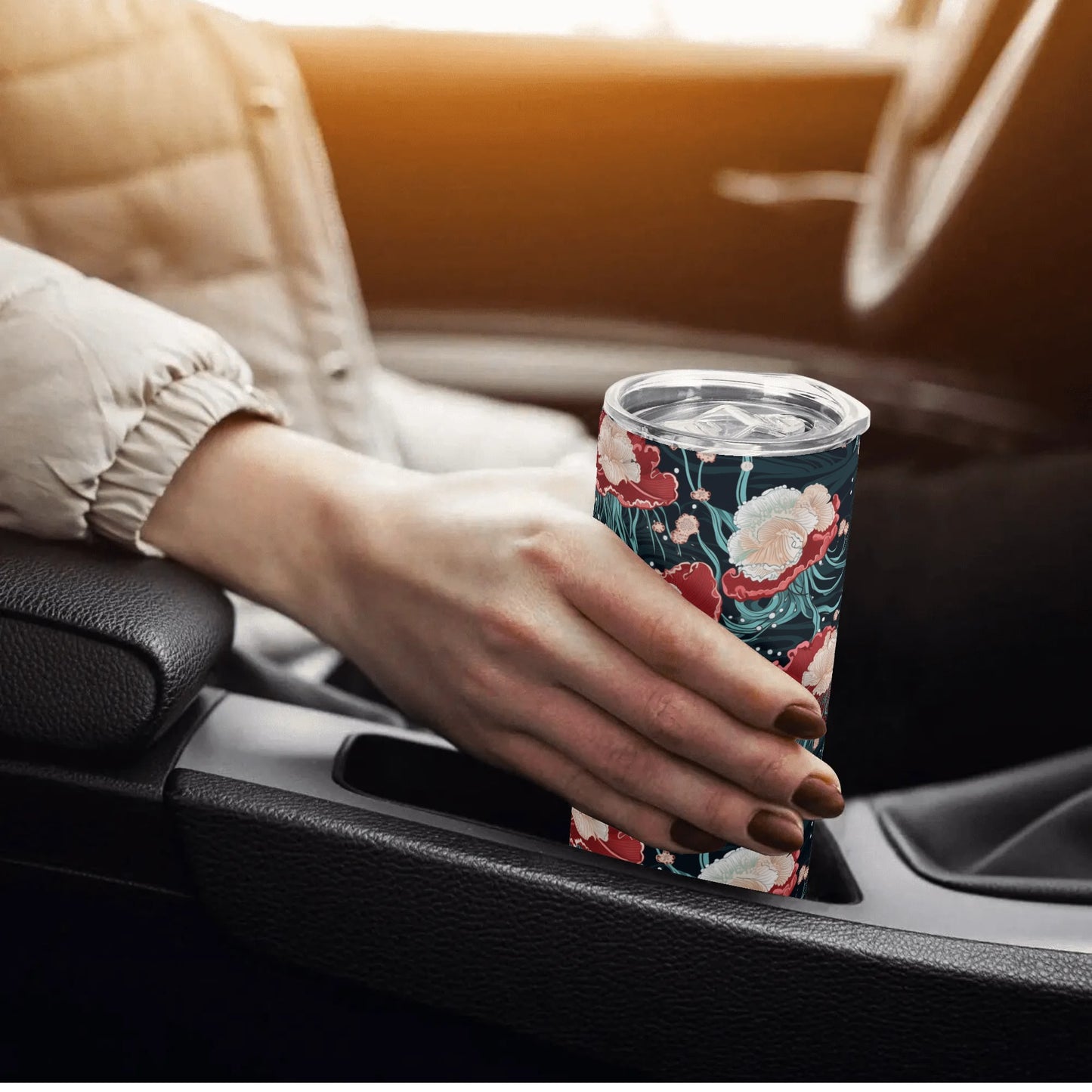 Hand holding a jellyfish floral-patterned tumbler in a car.
