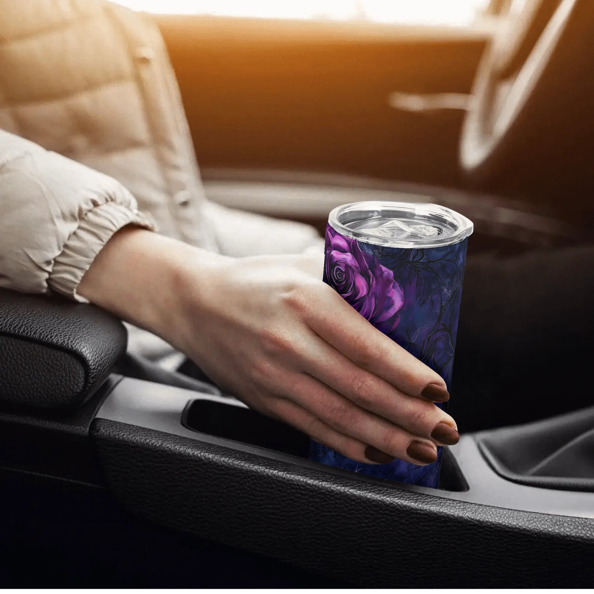 Hand holding a purple floral-patterned tumbler in a car.