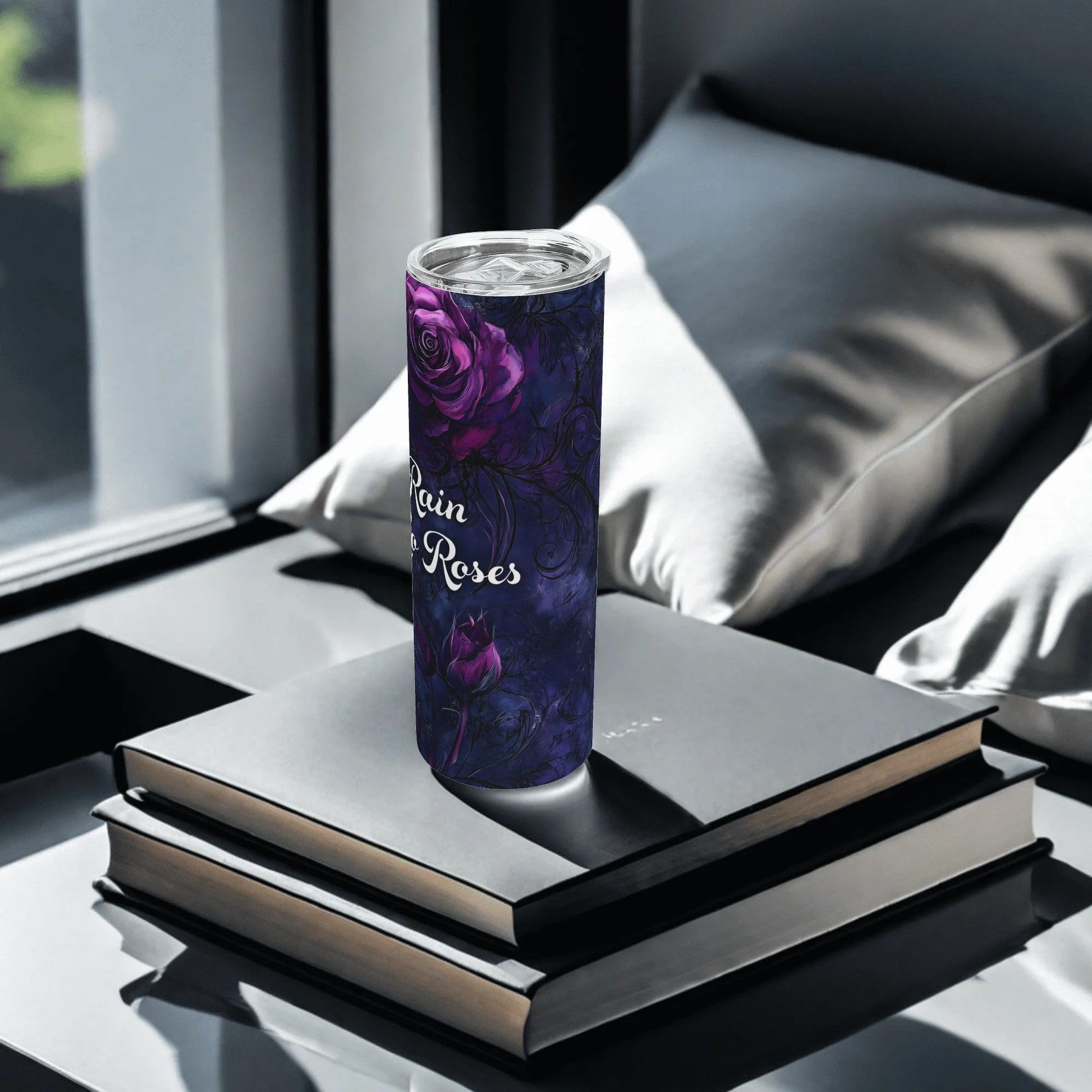 Tumbler with purple rose design and text "no rain, no roses" on a stack of books, placed on a reflective surface.