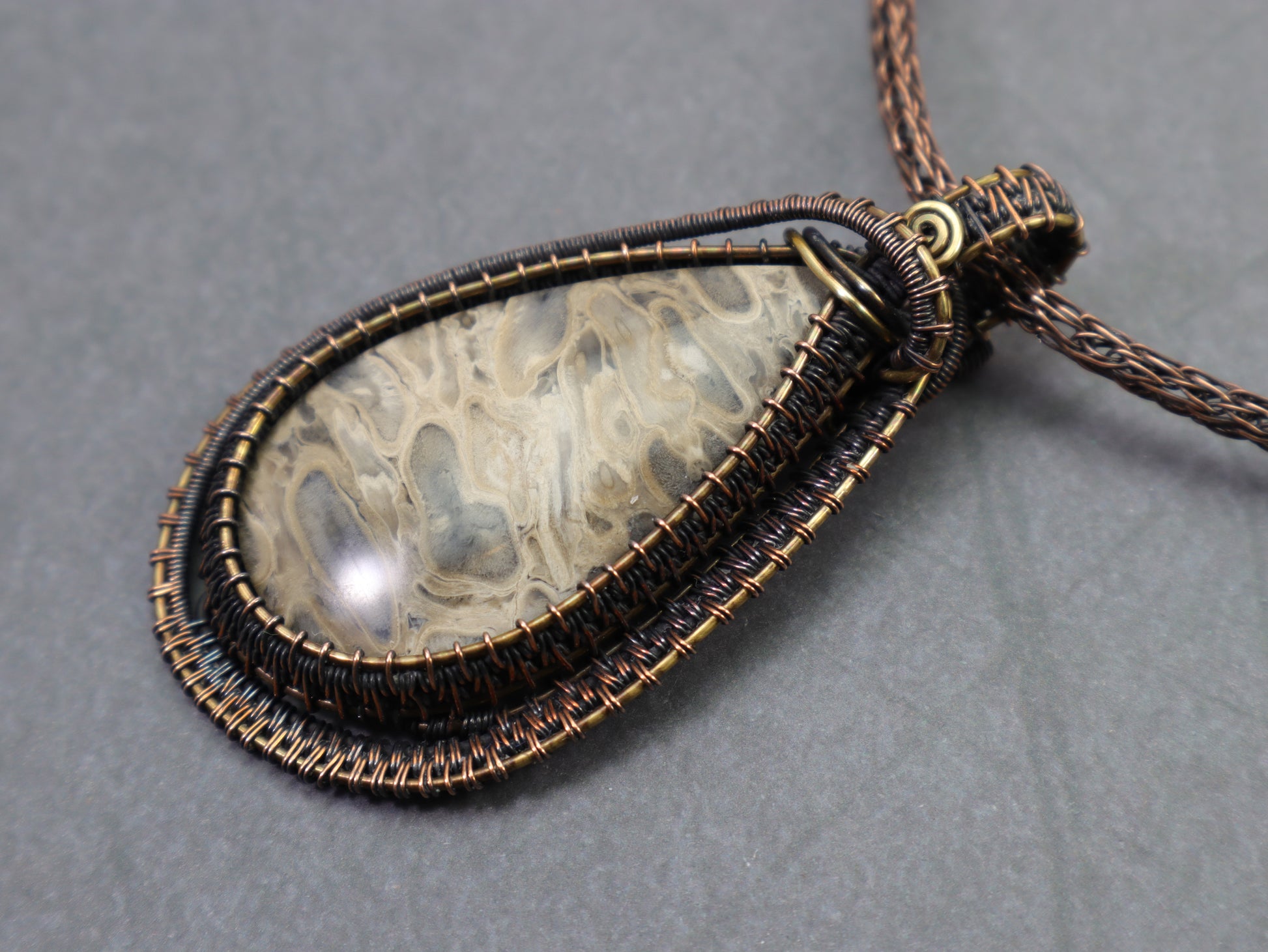 Front view of neutral colored petrified palmwood wire woven pendant with antiqued metal finish