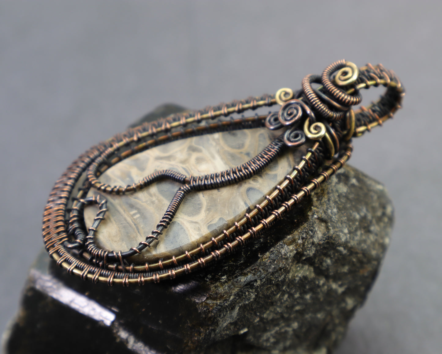 Back view of petrified palmwood pendant with whimsical art nouveau vine wire design sitting on a black tourmaline crystal.