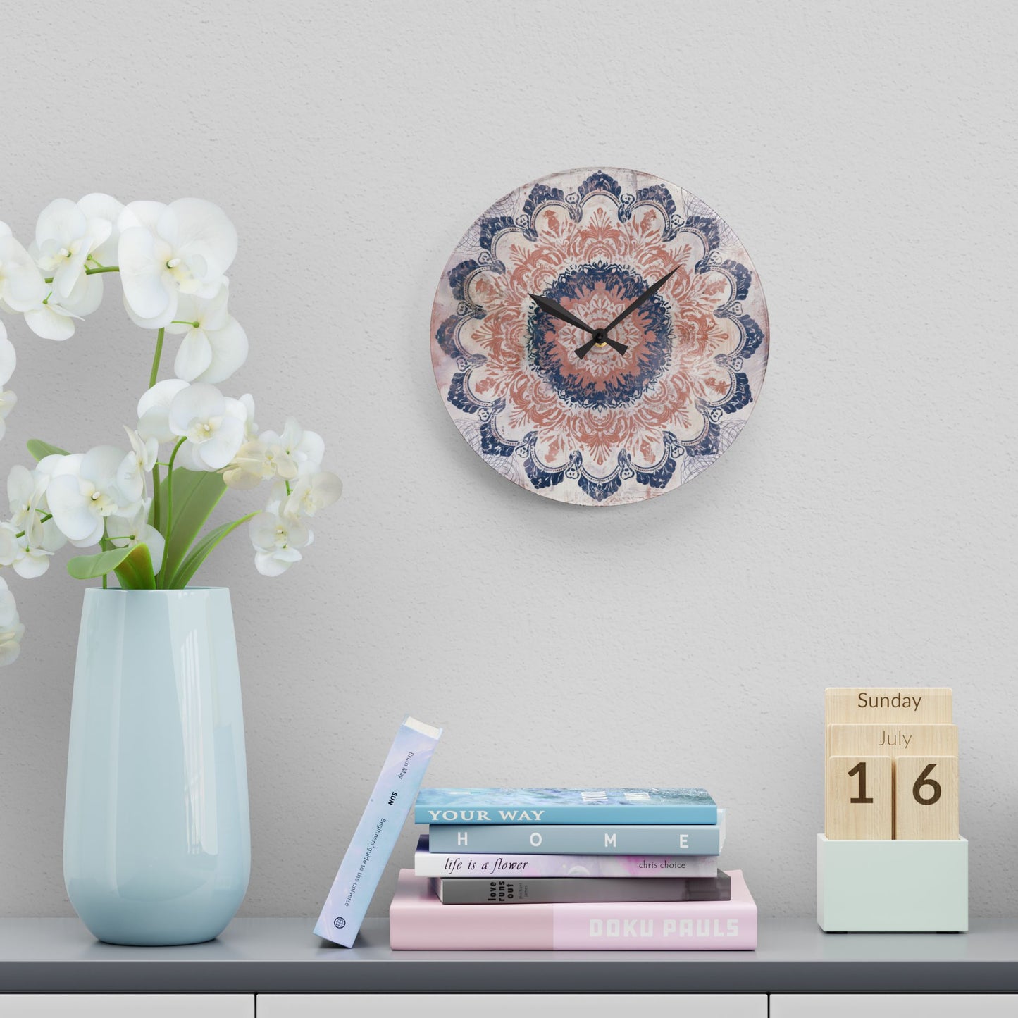 Round boho wall clock displayed above books and white flowers in minimalist room