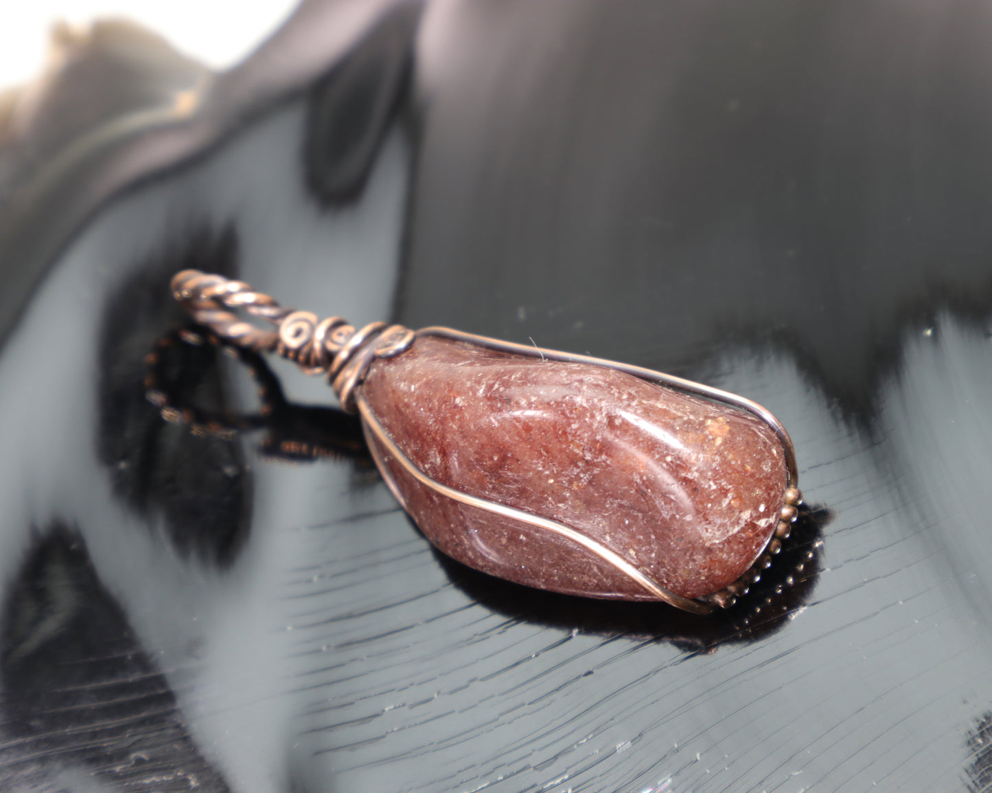 Red aventurine wire wrapped pendant in oxidized copper on black reflective surface