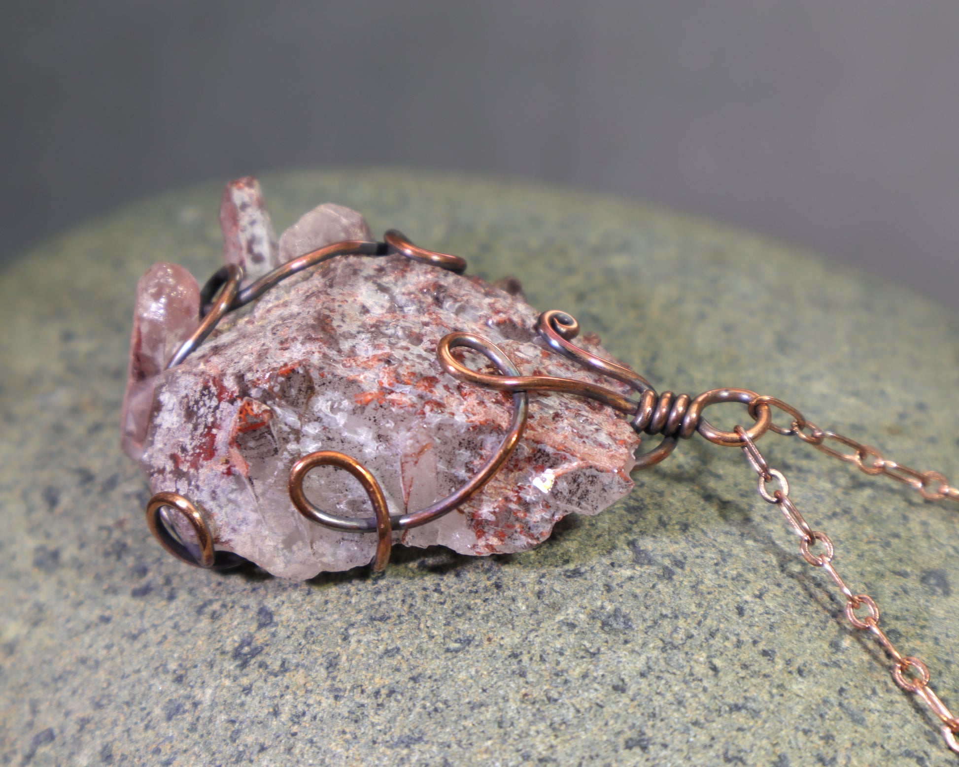 Raw quartz crystal cluster with red mineral inclusions and copper wrap