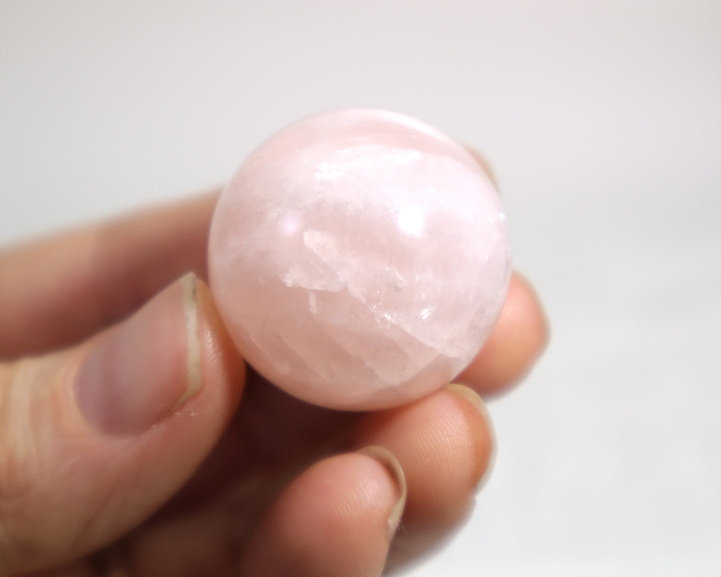 Rose quartz orb polished gemstone sphere close-up held between fingers on a white background