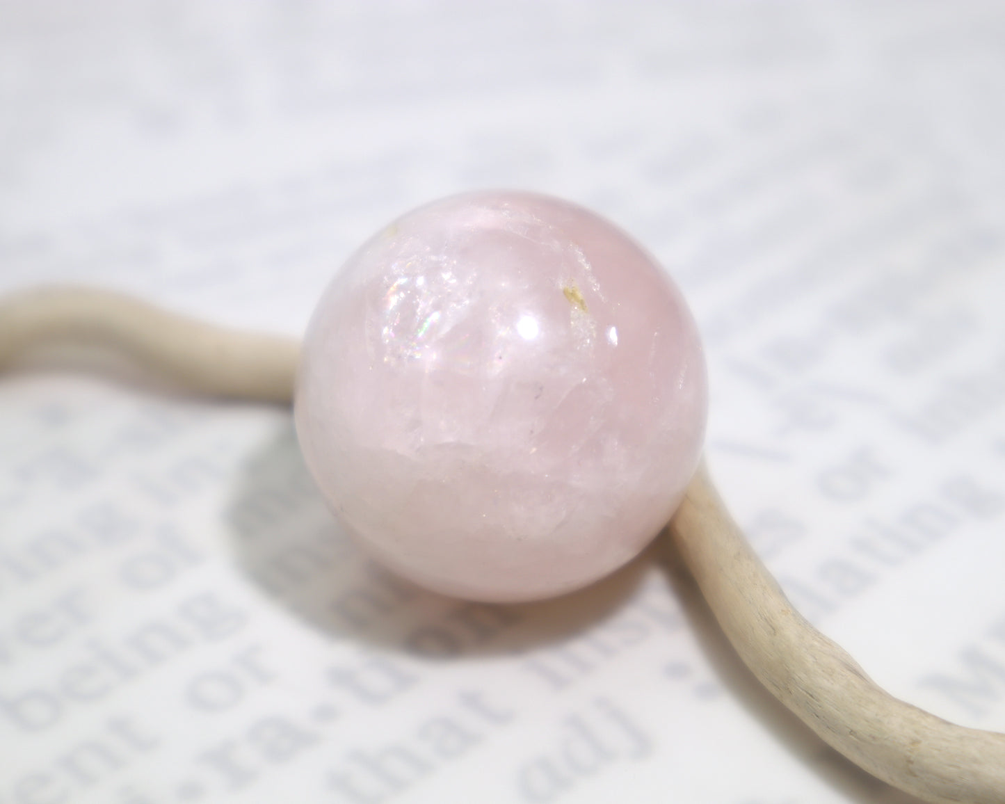 A polished rose quartz crystal sphere with internal veils sitting on a white background with a piece of wood