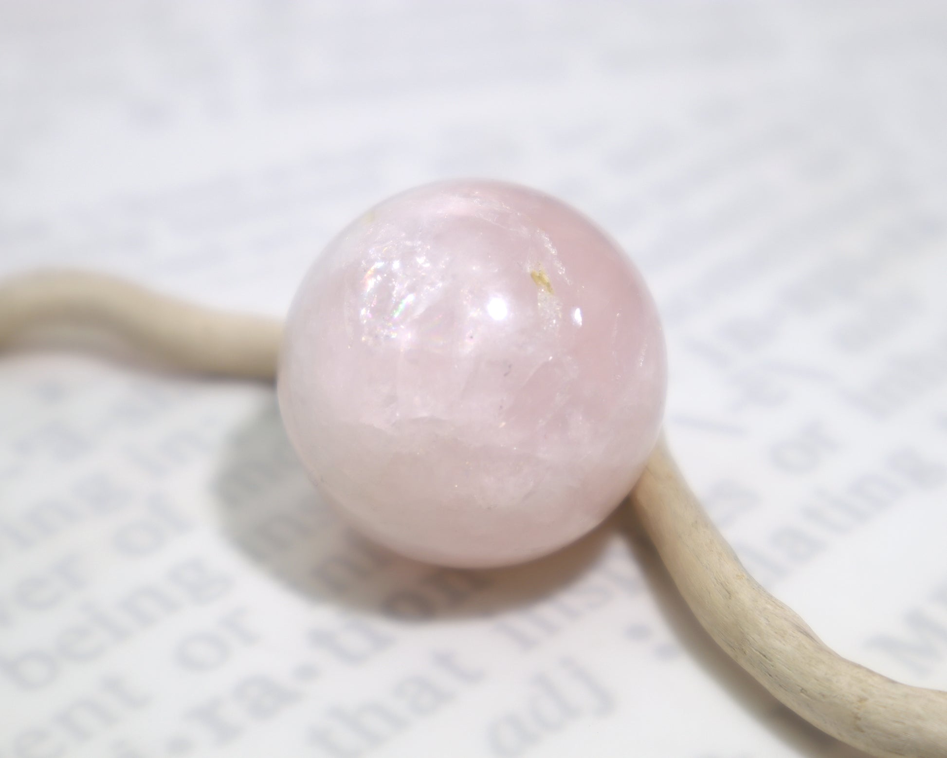 A polished rose quartz crystal sphere with internal veils sitting on a white background with a piece of wood