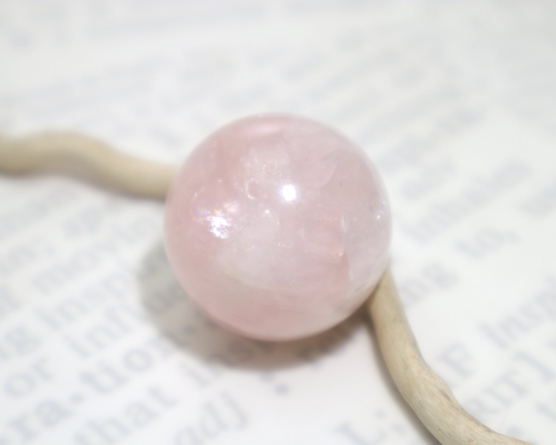 Medium sized rose quartz sphere for meditation and reiki sitting on a white background with a piece of driftwood
