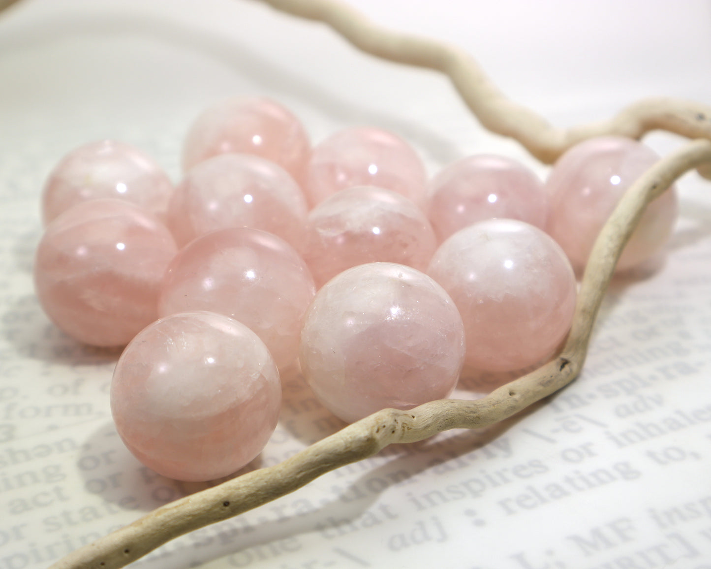 Pink rose quartz crystal marbles on a white surface with a driftwood branch.