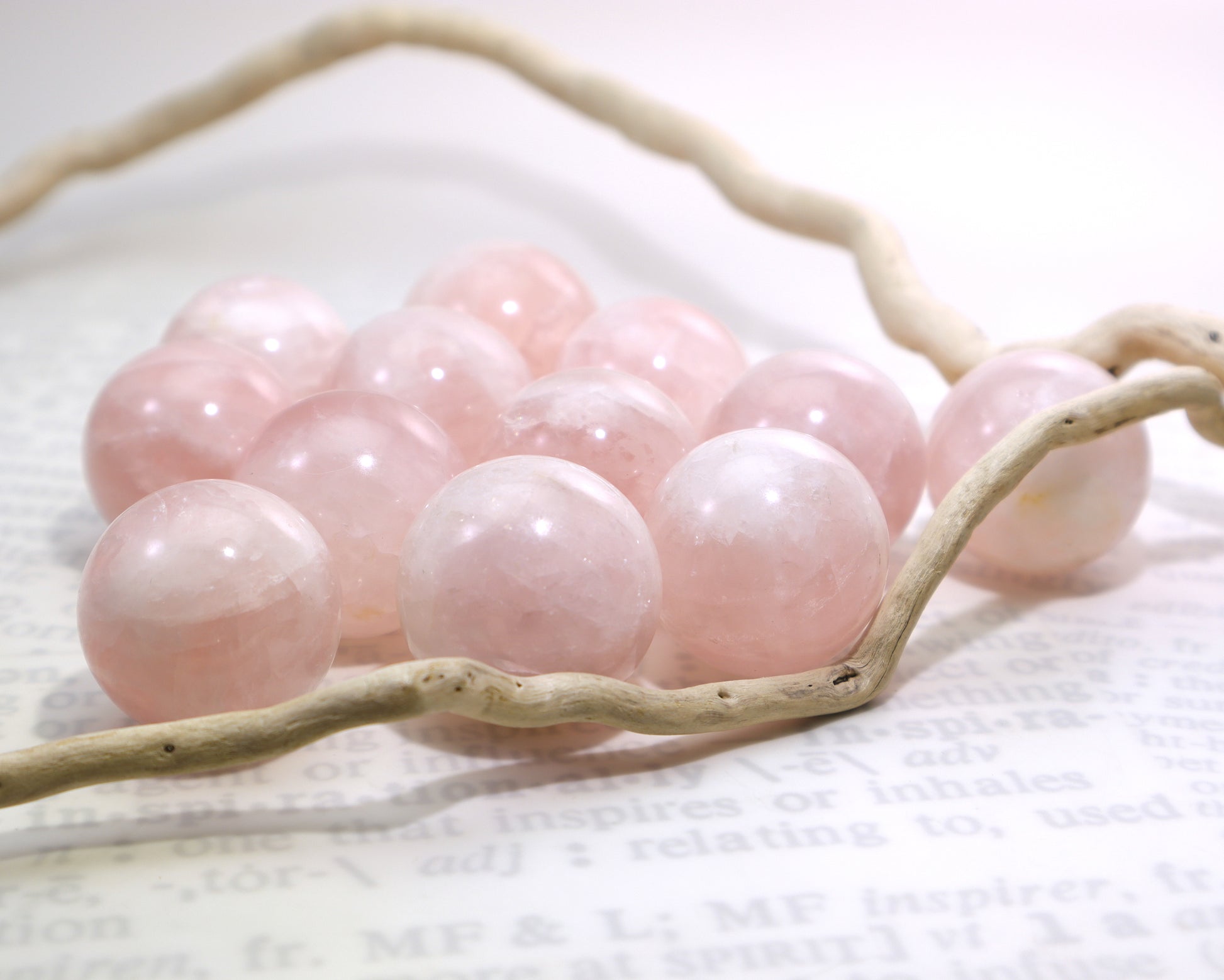 Pink rose quartz spheres on a white background with two pieces of driftwood.