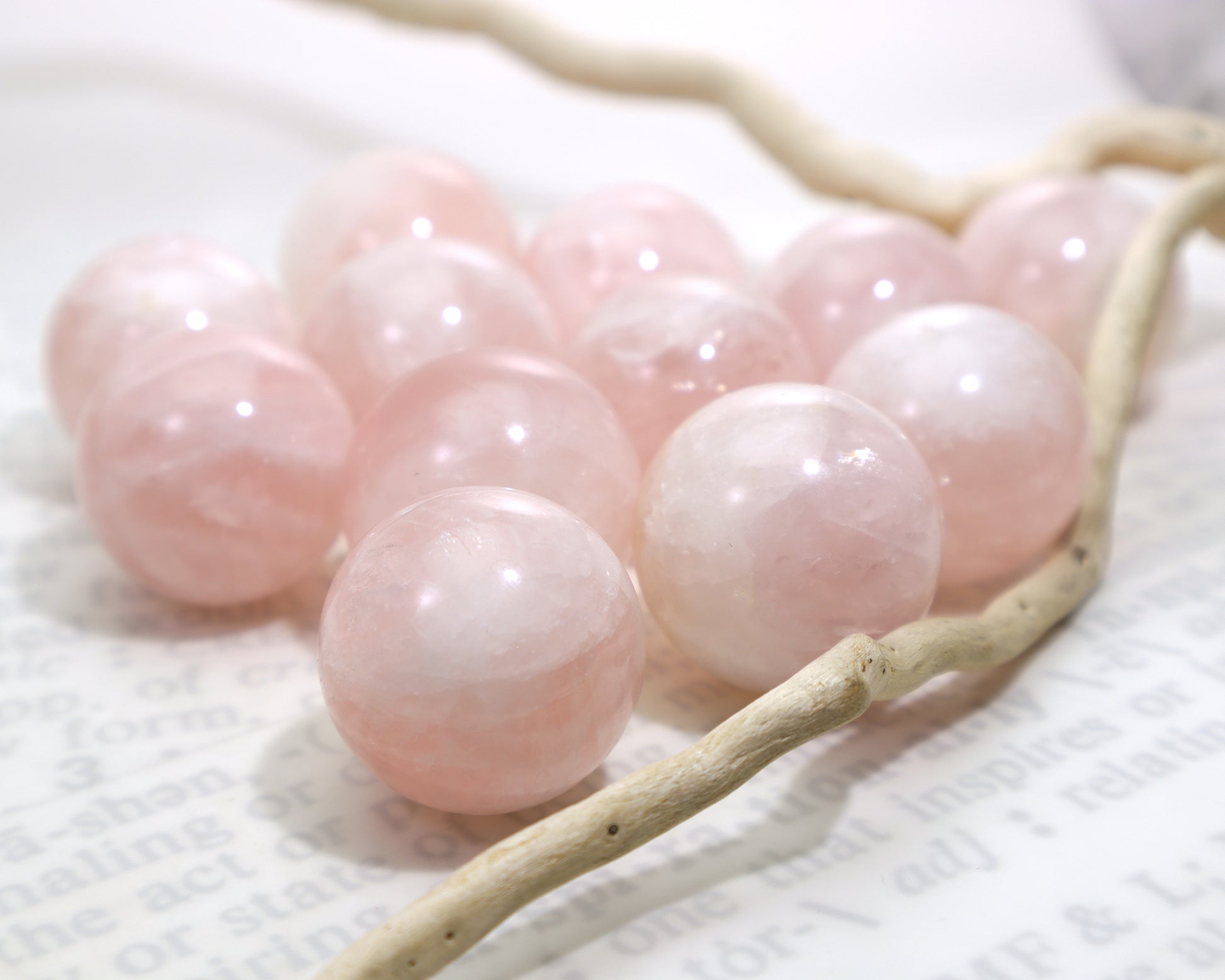 27–29mm rose quartz spheres with reflective inclusions on a white background next to driftwood