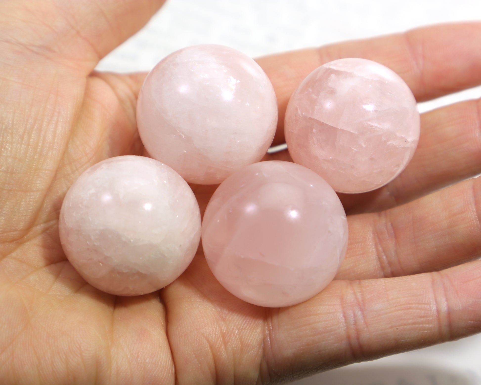 Four pink rose quartz gemstone spheres held in a hand against a neutral background